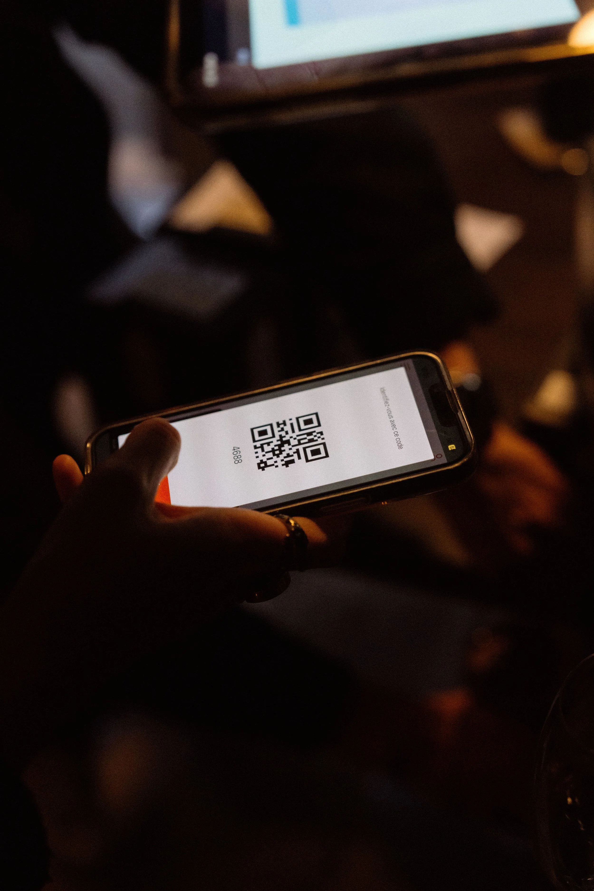 Une personne tient un smartphone affichant un code QR dans une pièce sombre.