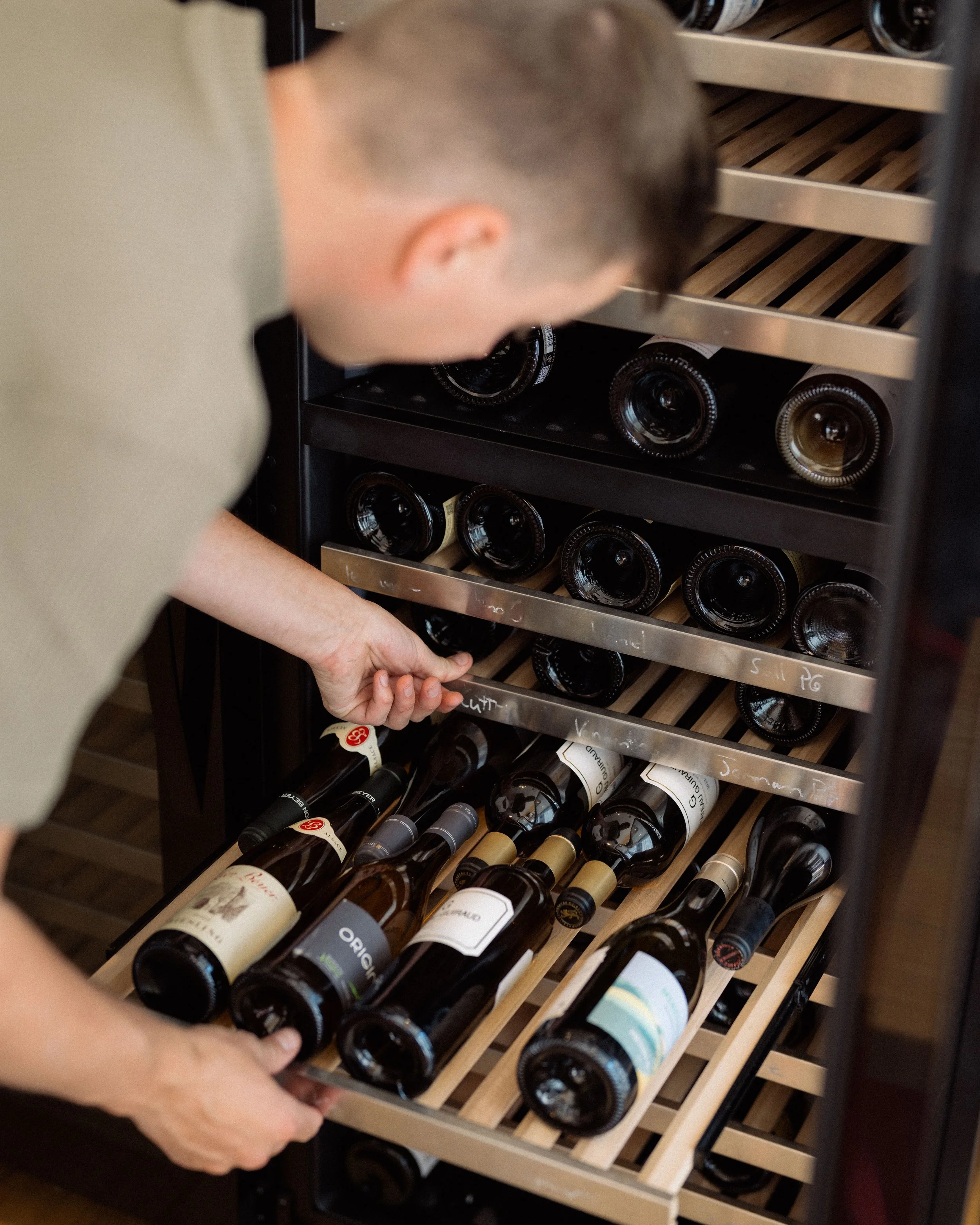 Personne qui choisit une bouteille de vin dans une cave à vin.