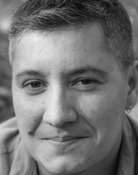 Close-up black and white photo of a person's face, smiling gently, with short hair and wearing an earring.