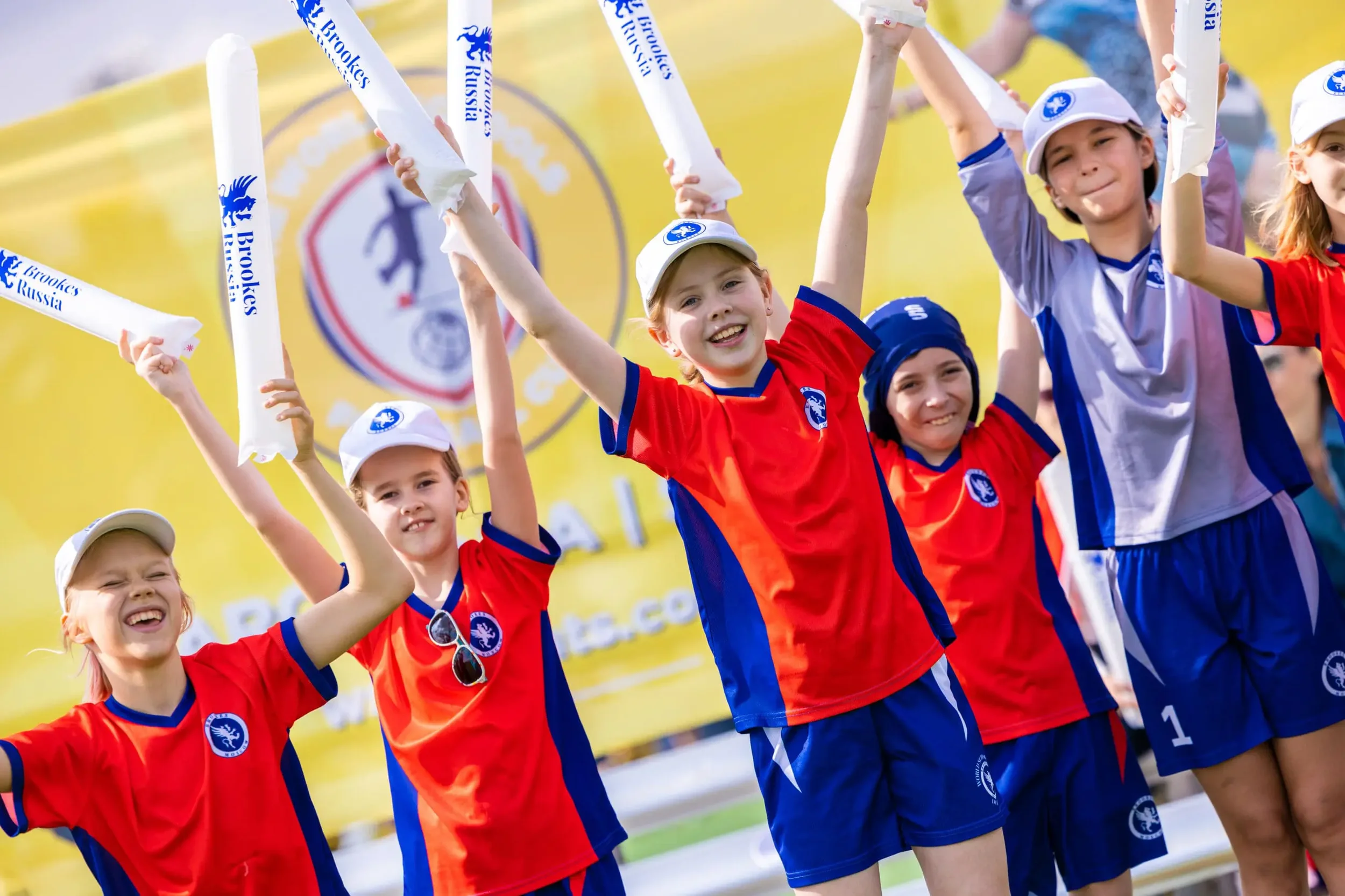 Children in sports uniforms celebrating and holding white sticks at an outdoor event.