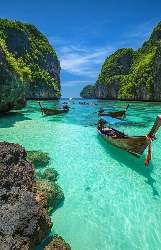 Tropical waterway with turquoise water, surrounded by tall green cliffs, with several traditional wooden boats floating on the water.