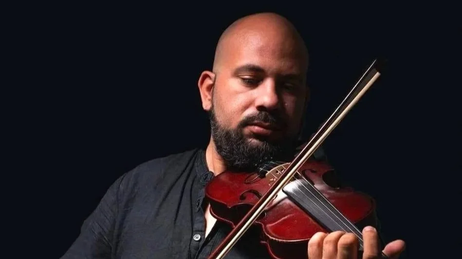 Man with a beard playing a violin against a dark background.
