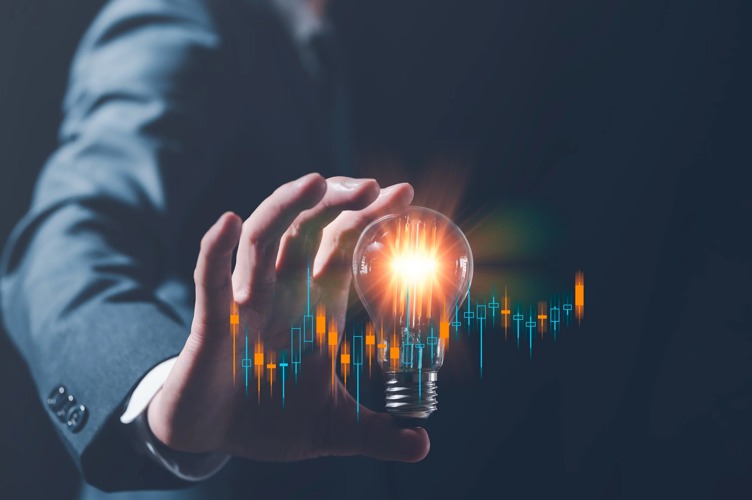 A person in a suit holding a glowing light bulb with digital graphs and charts overlaid, symbolizing innovation and technology.