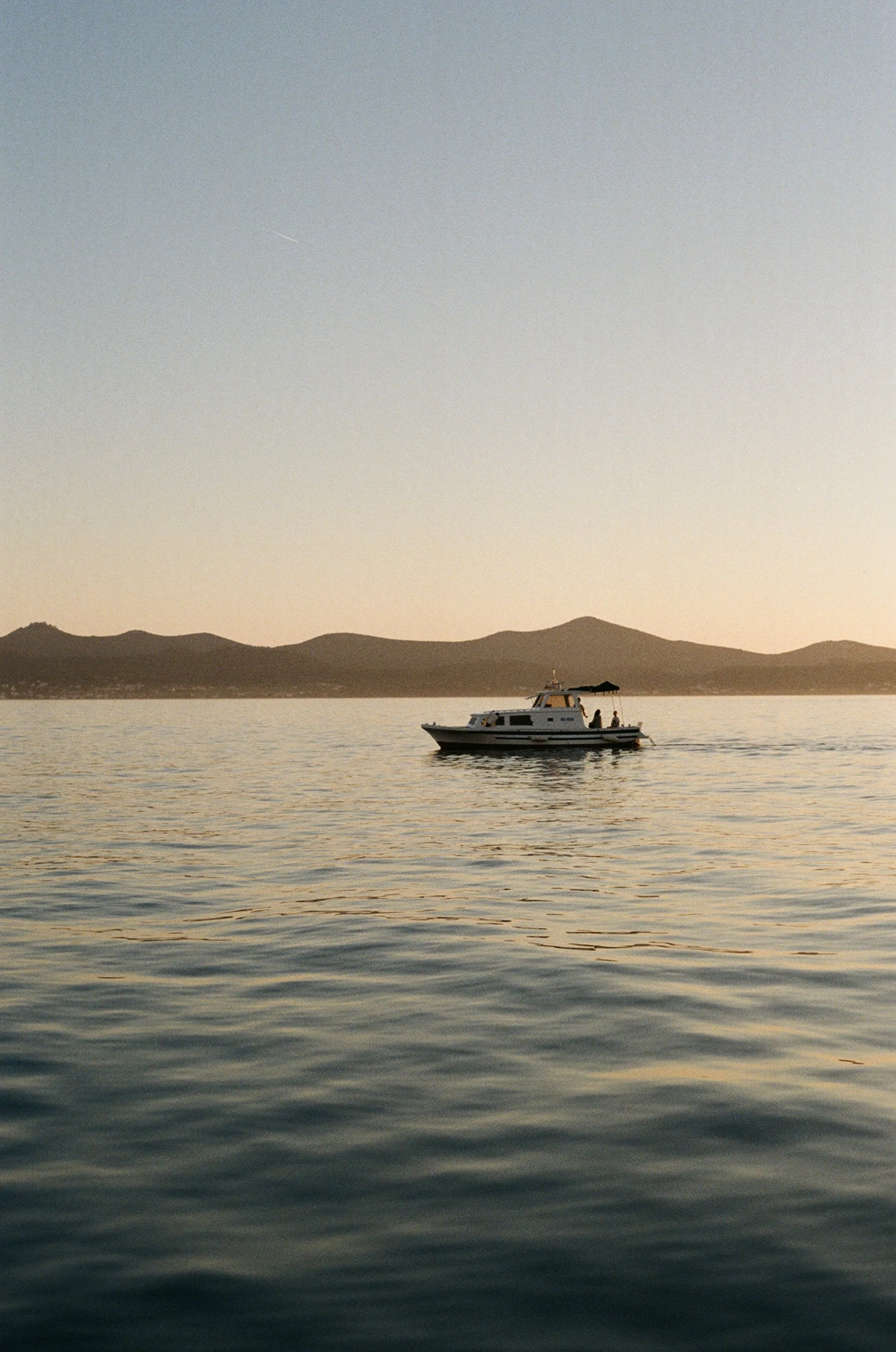 A boat on calm water during sunset with mountains in the background.