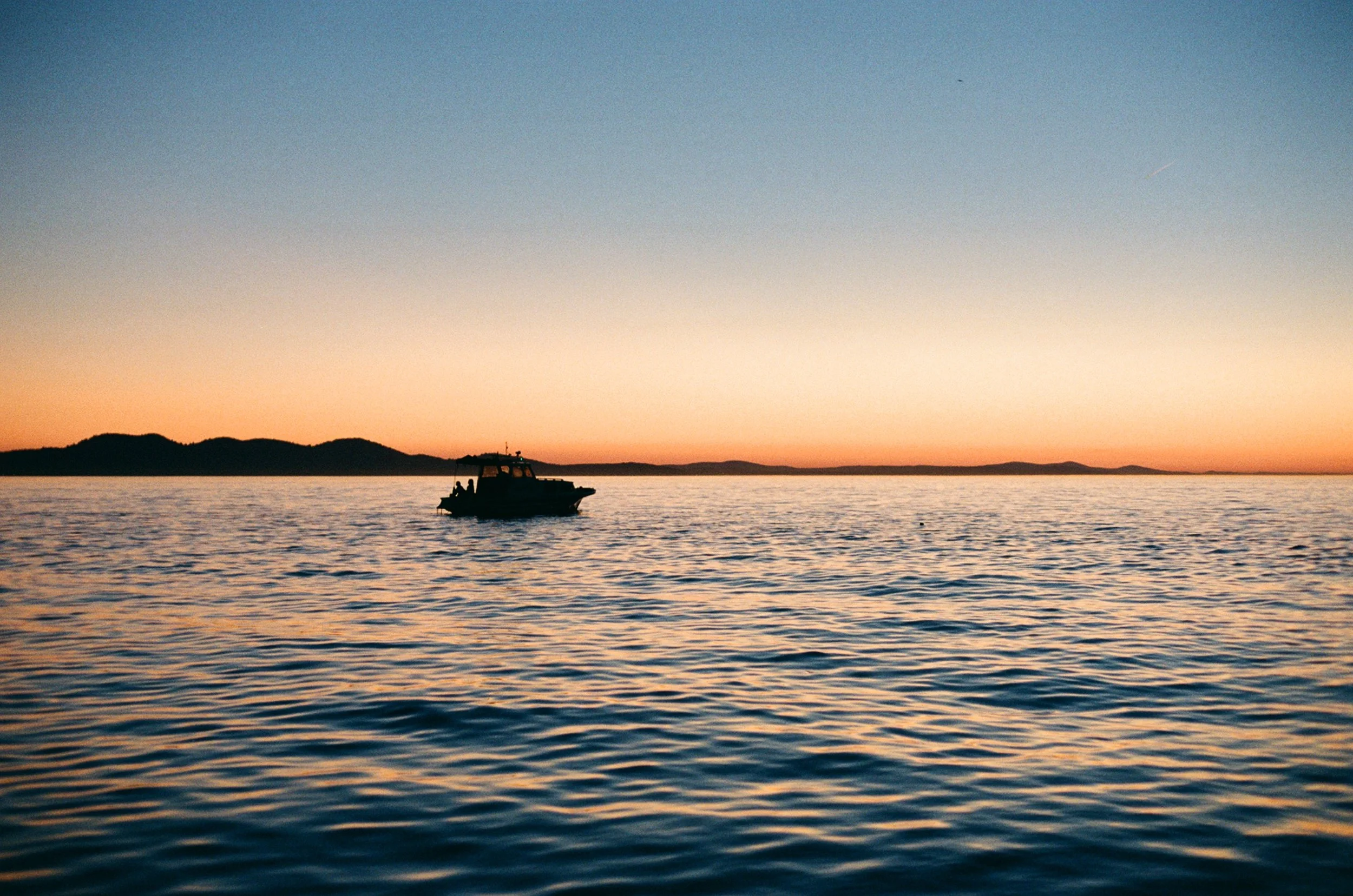 A boat floating on calm water during sunset with a ridge of land in the distance.