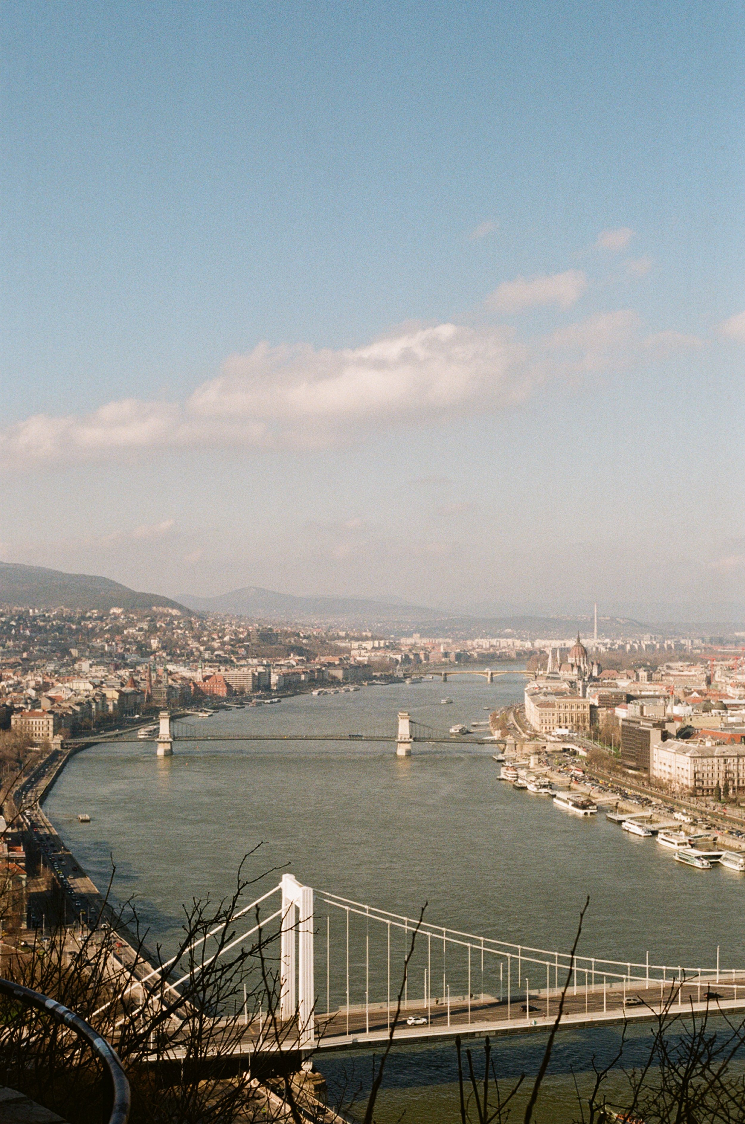 Aerial view of the Danube River with chain bridge in Budapest, Hungary, showing cityscape, bridges, and boats on the water.