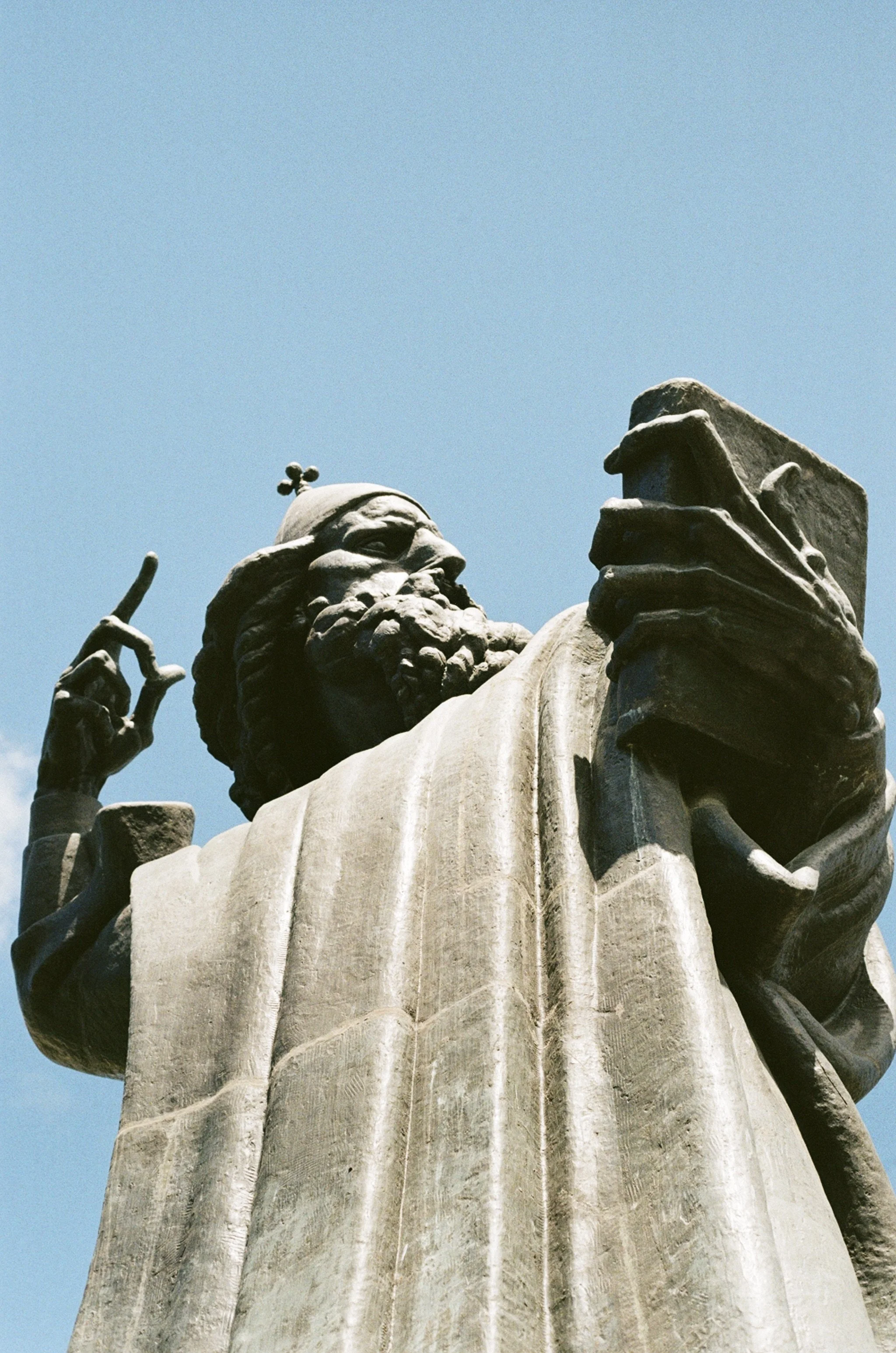 Close-up of the Martin Luther King Jr. statue, showing his face, beard, and his right hand raised with a finger pointing upward, against a clear blue sky.