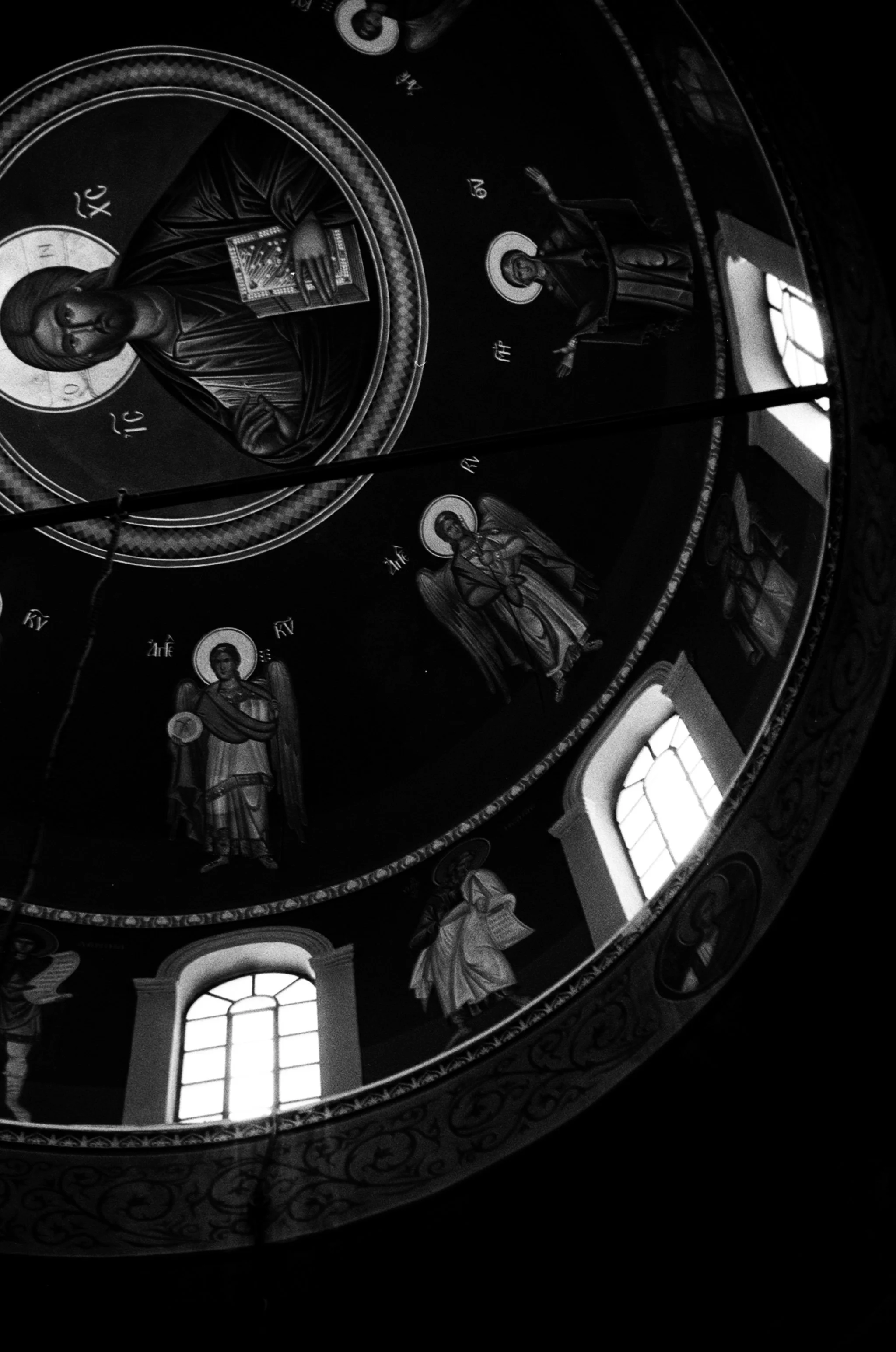 Black and white photograph of a religious ceiling mural with icons of saints and Christ, framed by decorative patterns, with arched windows letting in light.