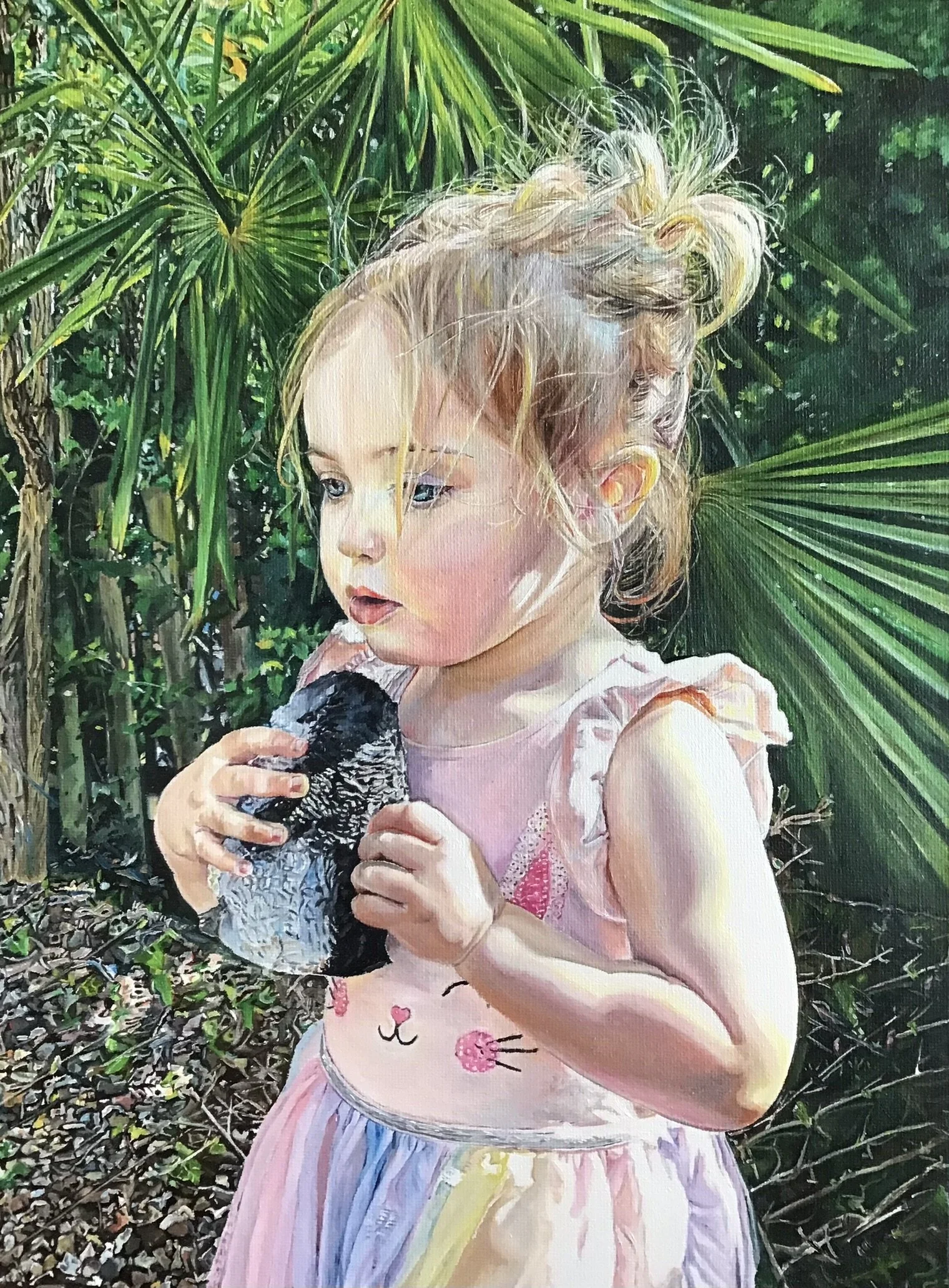 A young girl with blonde curly hair holding a small bird, standing amidst green tropical plants.