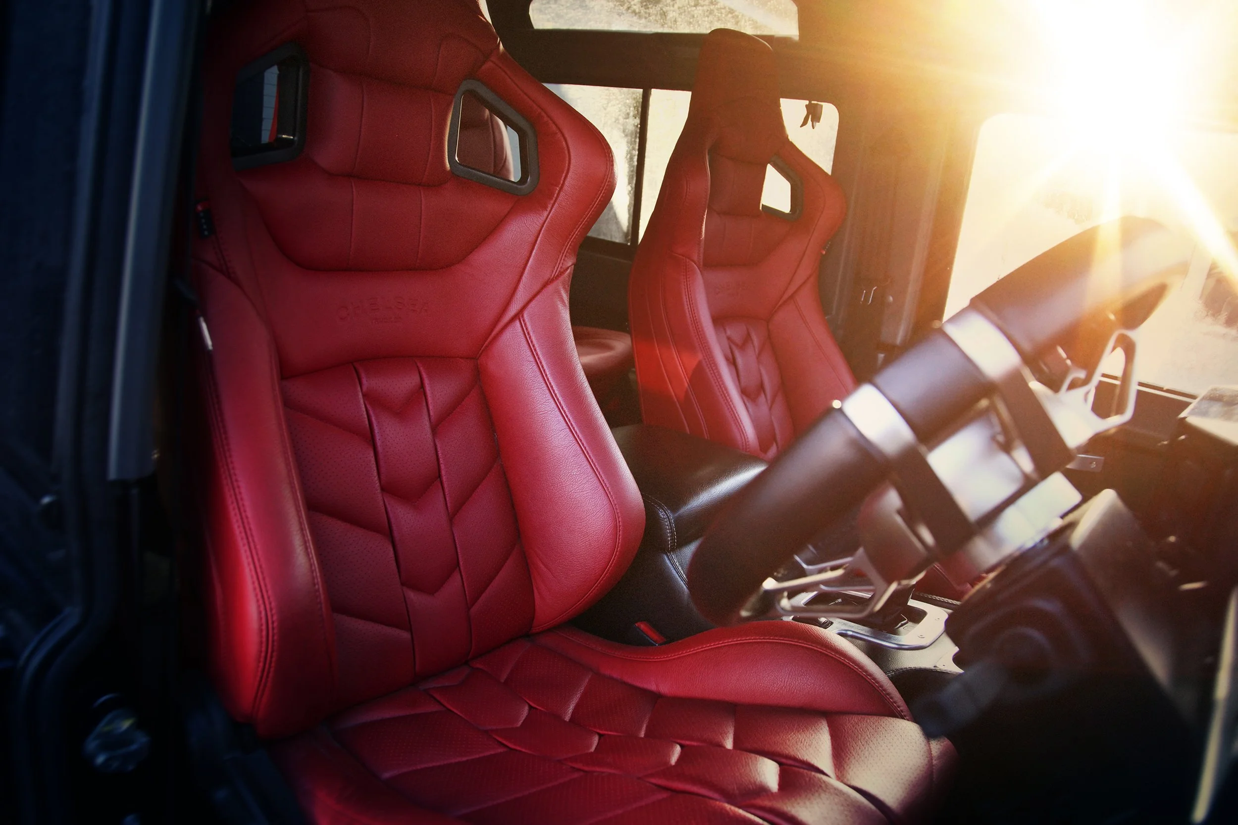 Inside view of a Project Kahn Land Rover Defender End Edition with red leather racing seats and a black steering wheel, sunlight shining through the windshield.