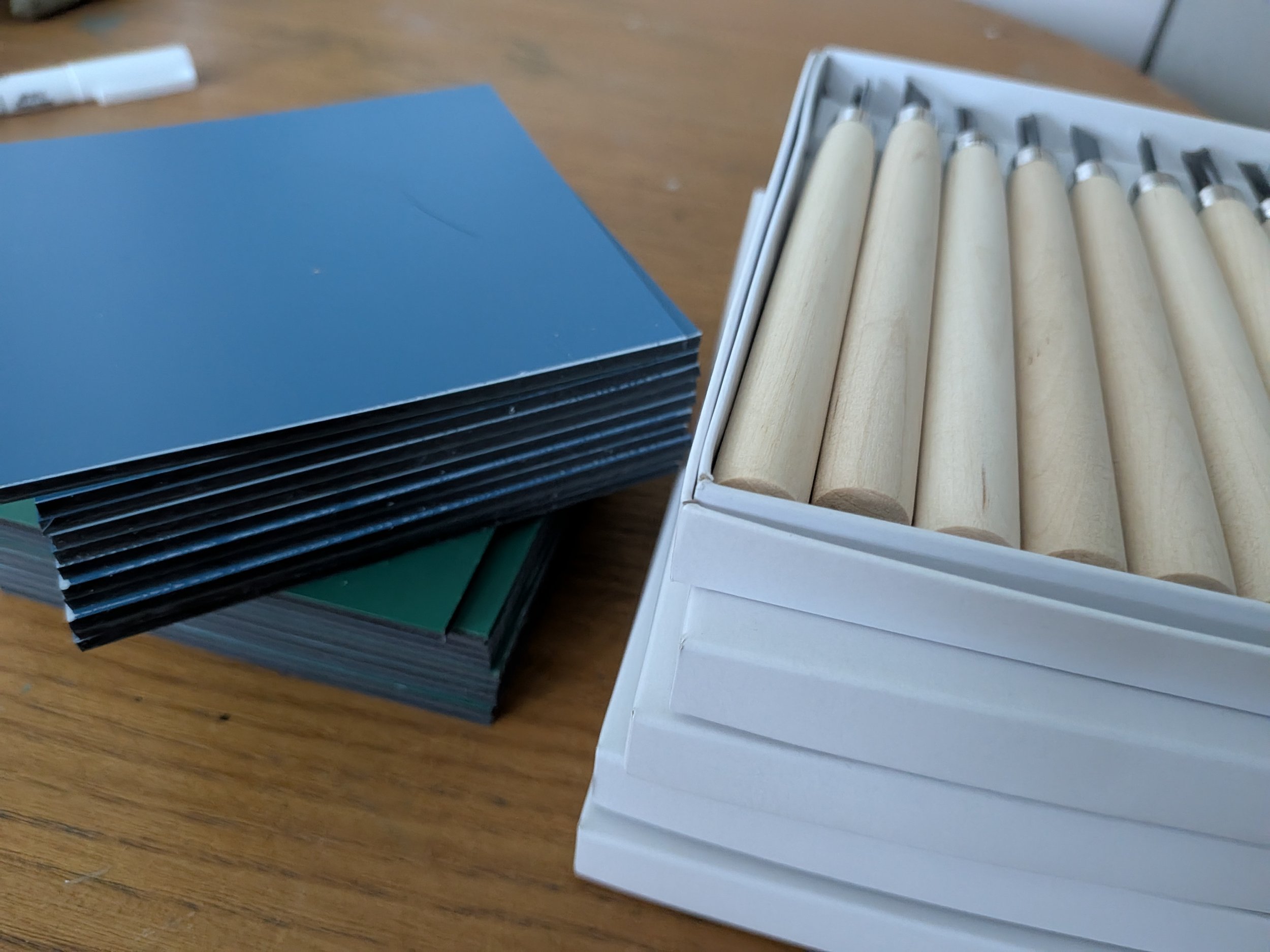 Open box of wooden-handled carving tools beside stacked blue notebooks on a wooden table