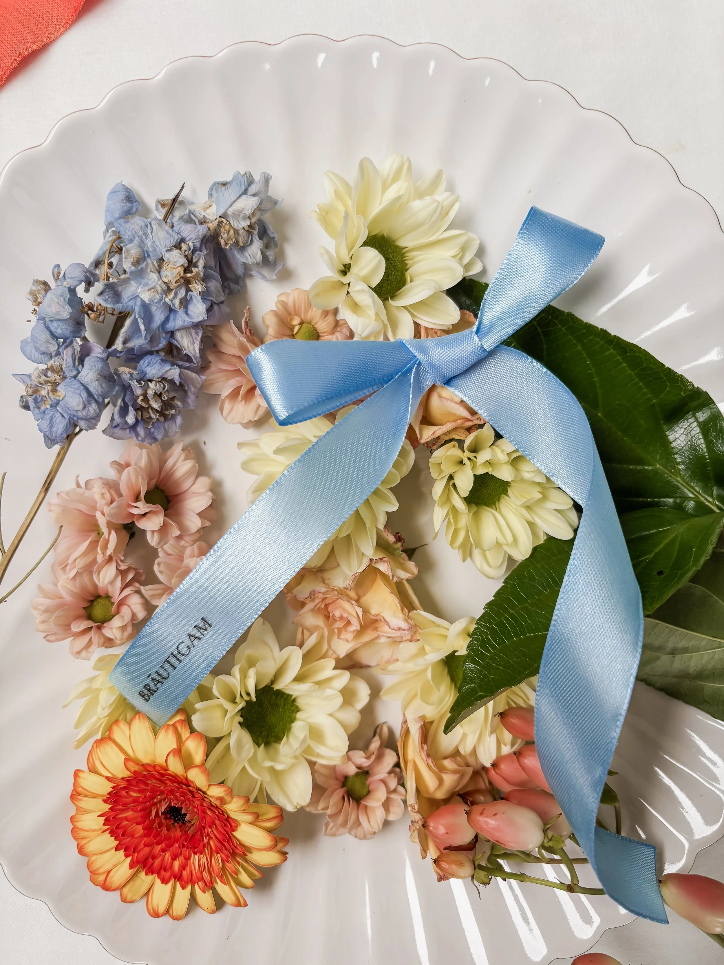 Blumenstrauß mit Wiesenblumen, mit einer blauen Schleife und darauf Gästenamen, auf einer weißen Platte