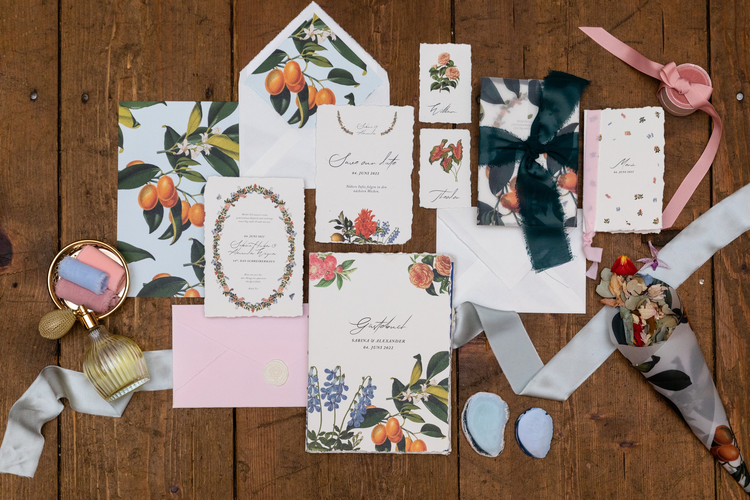 Hochzeitspapeterie Set auf Büttenpapier mit Einladungen, Ribbon, Geschenkverpackungen, Kerzen und Dekorationen auf einem Holztisch. Dekoriert mit vintage Blumen Illustrationen.