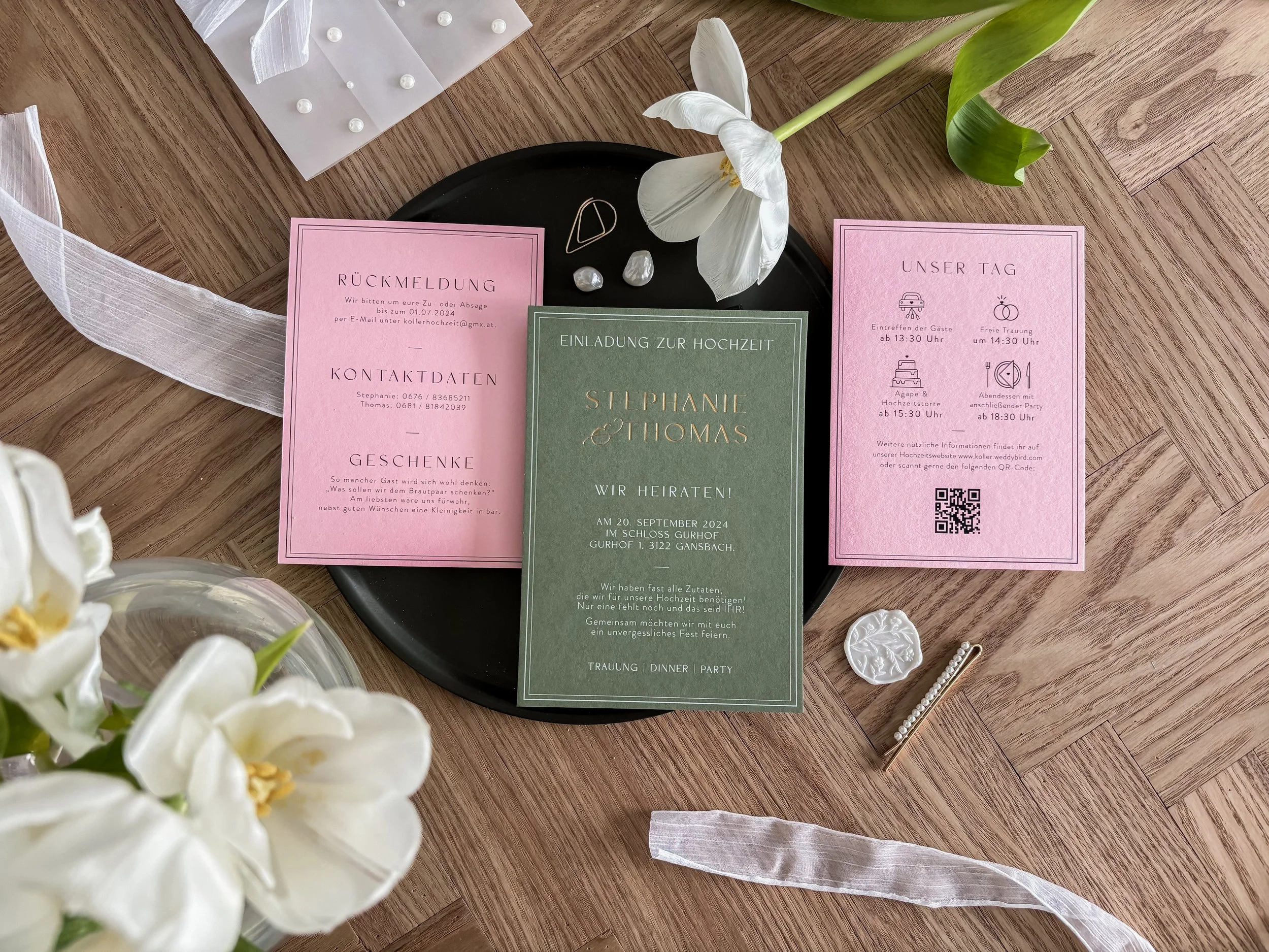 Hochzeits-Einladungskarten mit Goldener Schrift auf Grün und Rosa Papier, Blumen, Haarspange, Strassnadel, Deko-Buttons und weißen Stoffbändern auf Holztisch