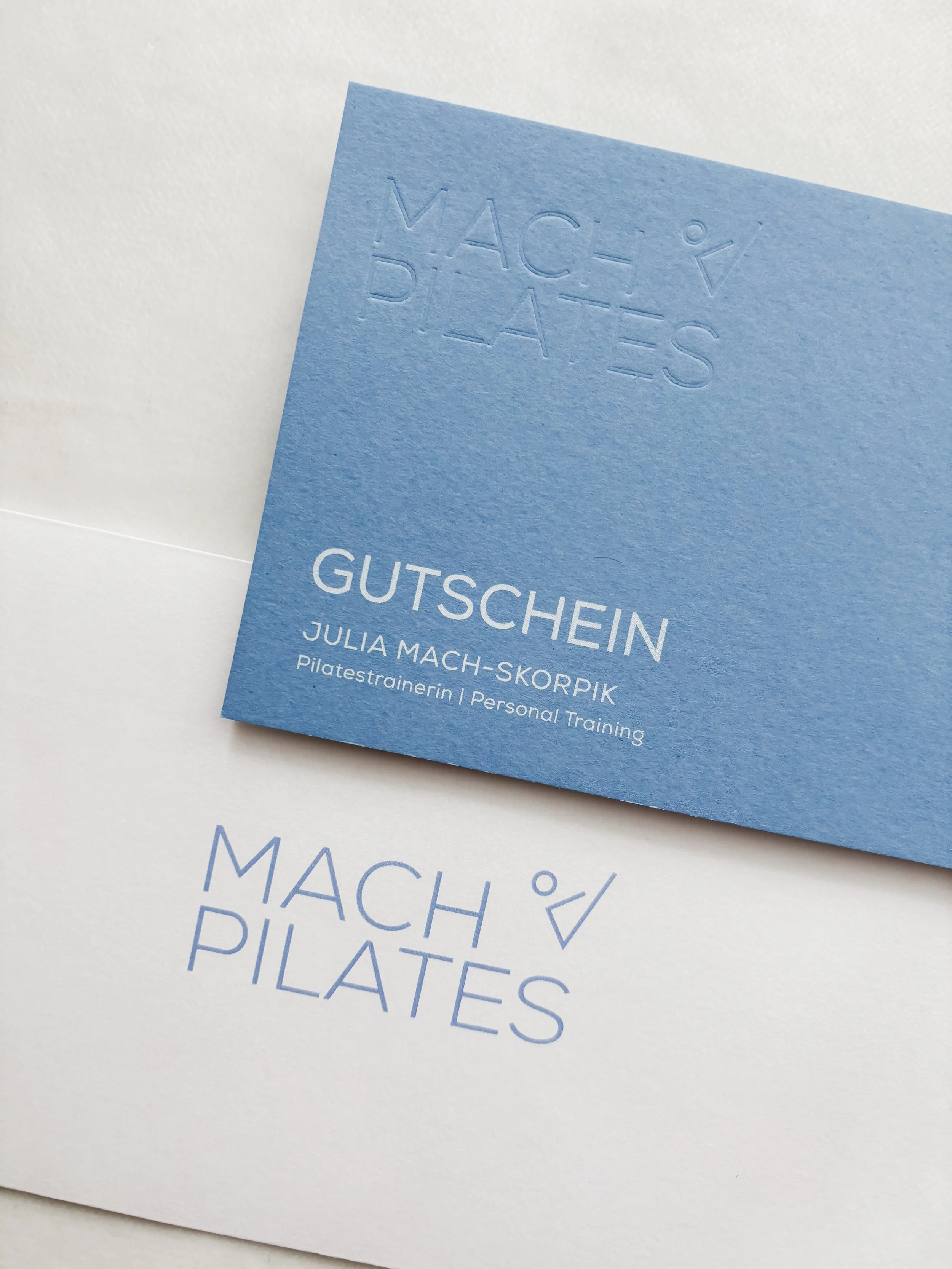 Gutschein für Julia Mach-Skorpik, Personal Trainerin, mit Texten zu Macha Pilates auf blauer und weißer Karte.