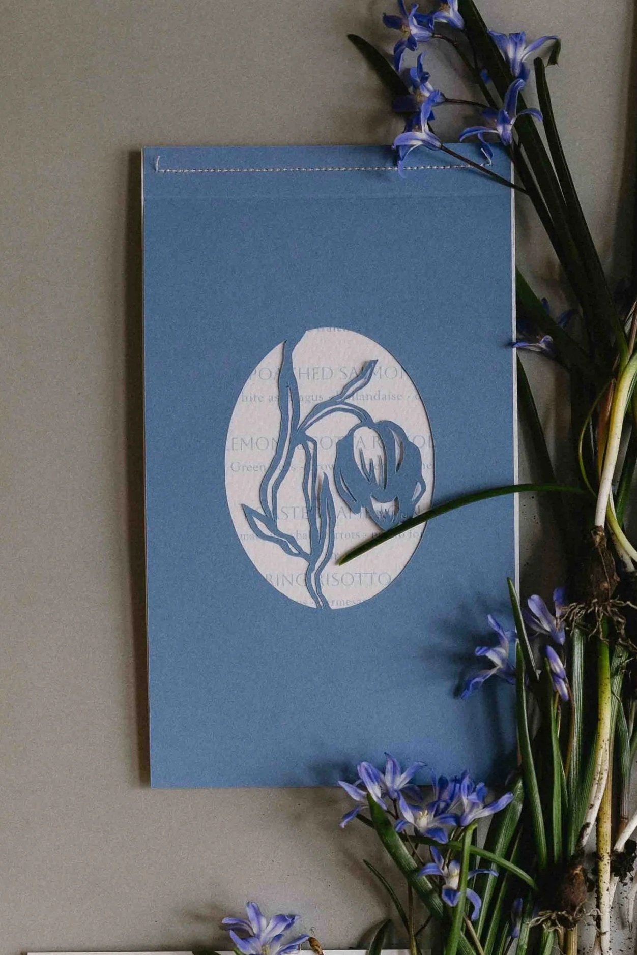Blumenstrauß mit blauen und weißen Blumen neben einer blauen Karte mit einer weißen ovalen Fläche und blauen Blumenelementen.