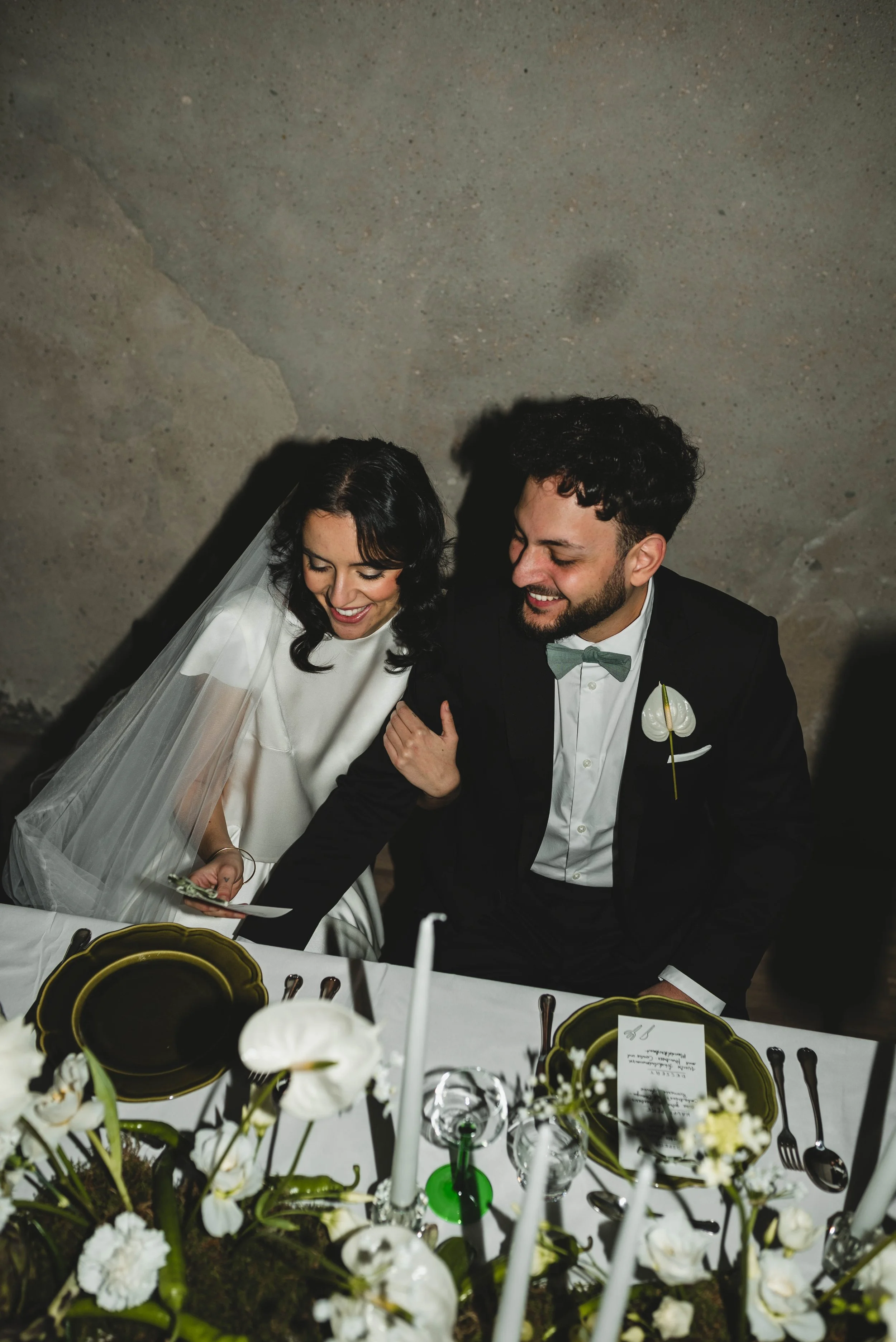 Ein glückliches Brautpaar bei ihrer Hochzeit, sitzend an einem festlich gedeckten Tisch mit Blumen und Kerzen.