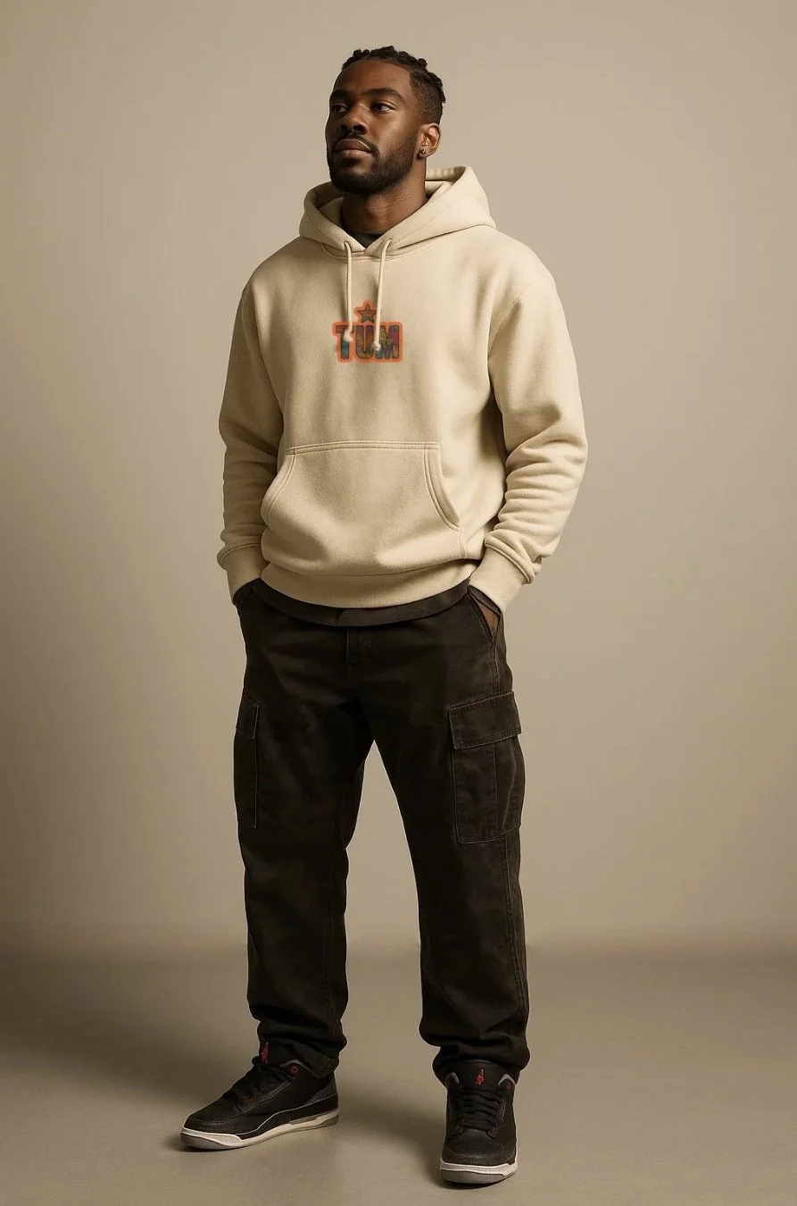 Man wearing beige hoodie with logo, black cargo pants, and black sneakers, standing against plain beige background.