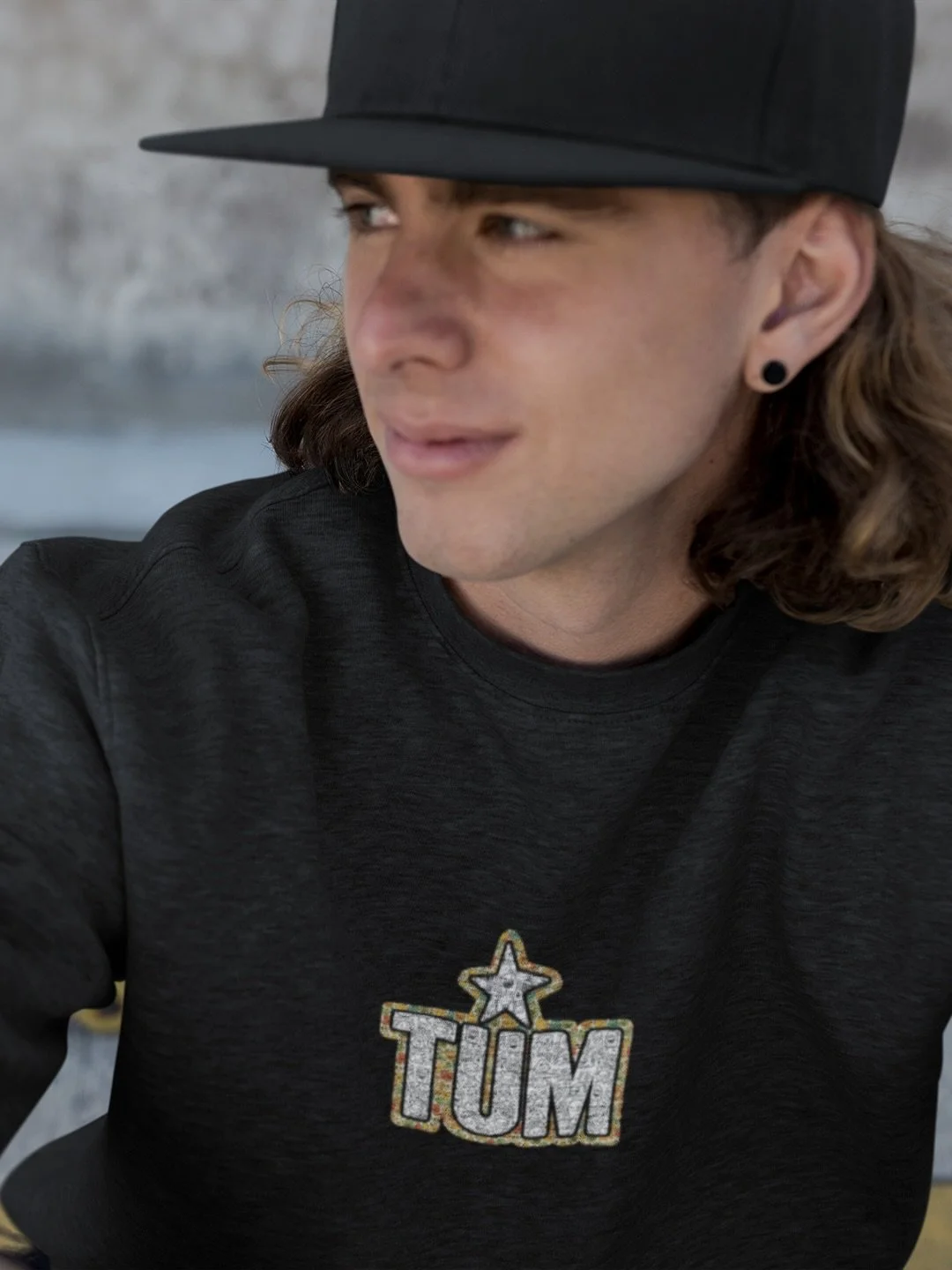Model wearing black TUM T-shirt with star logo and cap, looking to the side.