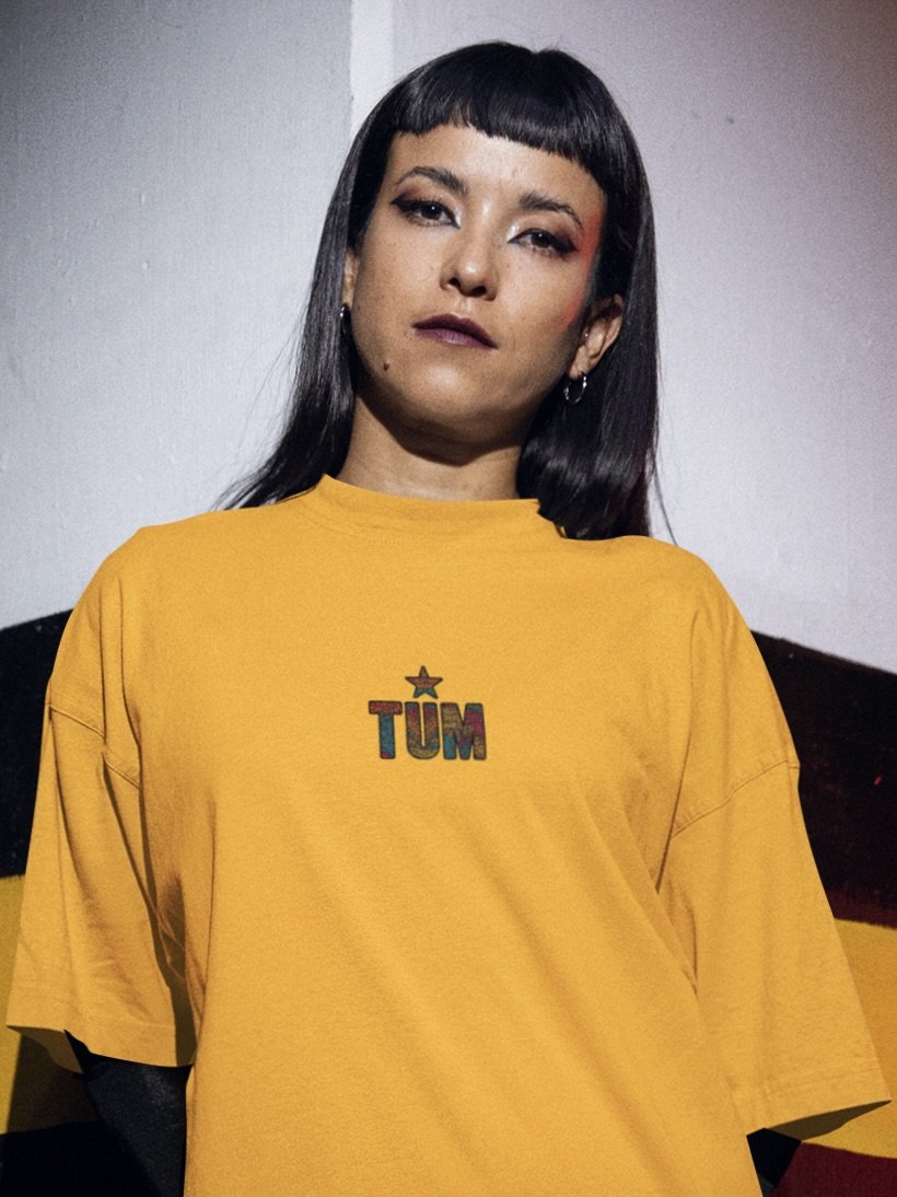 Model wearing yellow TUM T-shirt featuring star logo, minimalist background.