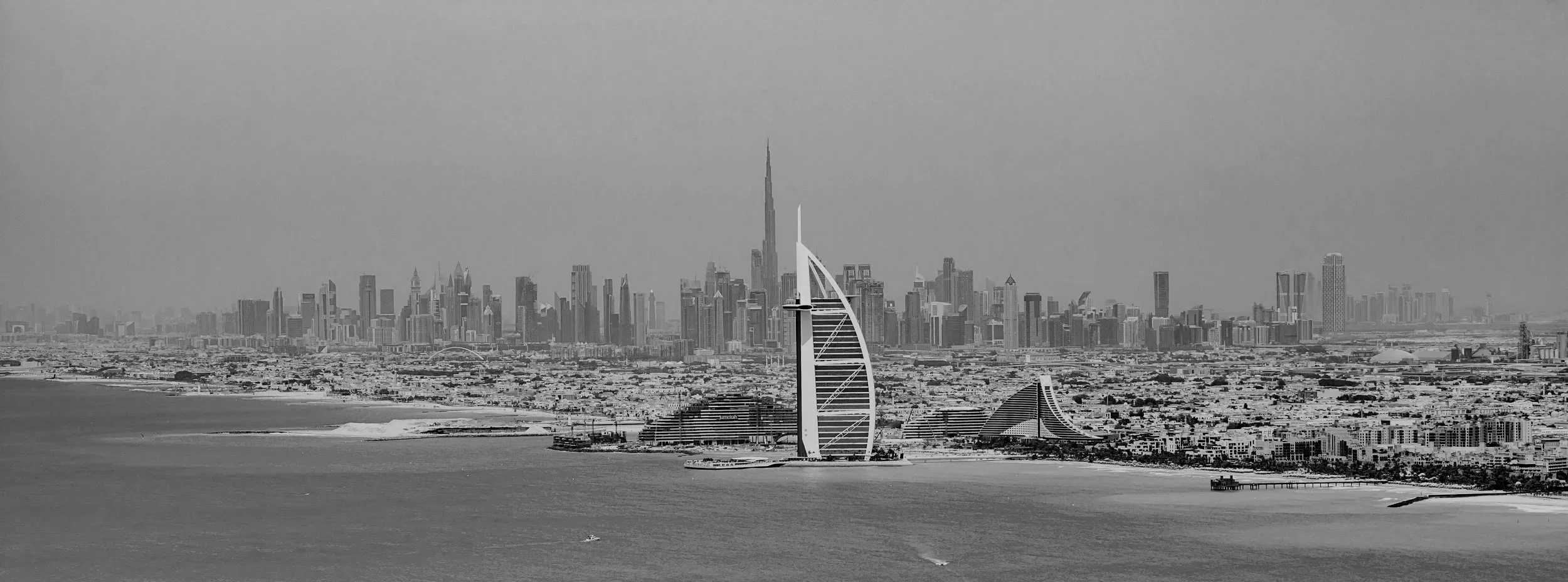 Black and white aerial view of Dubai skyline featuring the Burj Khalifa and the Burj Al Arab hotel.
