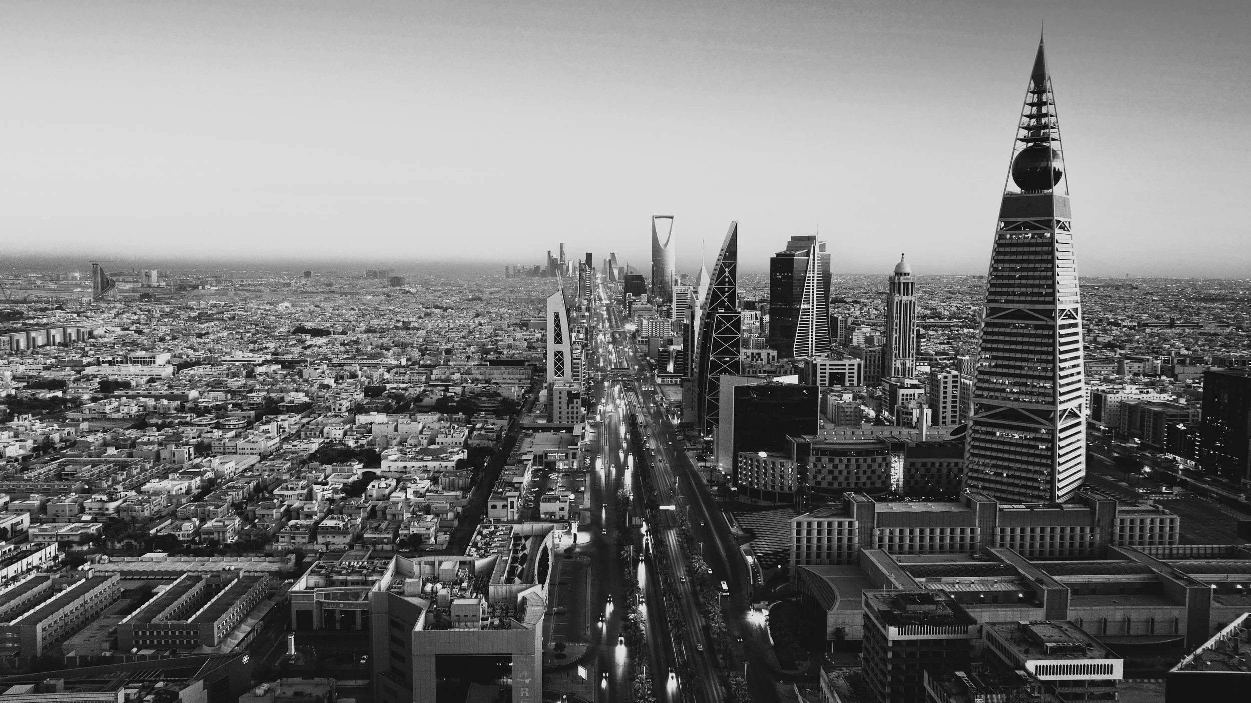 A black and white aerial view of a city skyline featuring tall skyscrapers along a busy highway, with buildings extending into the distance.