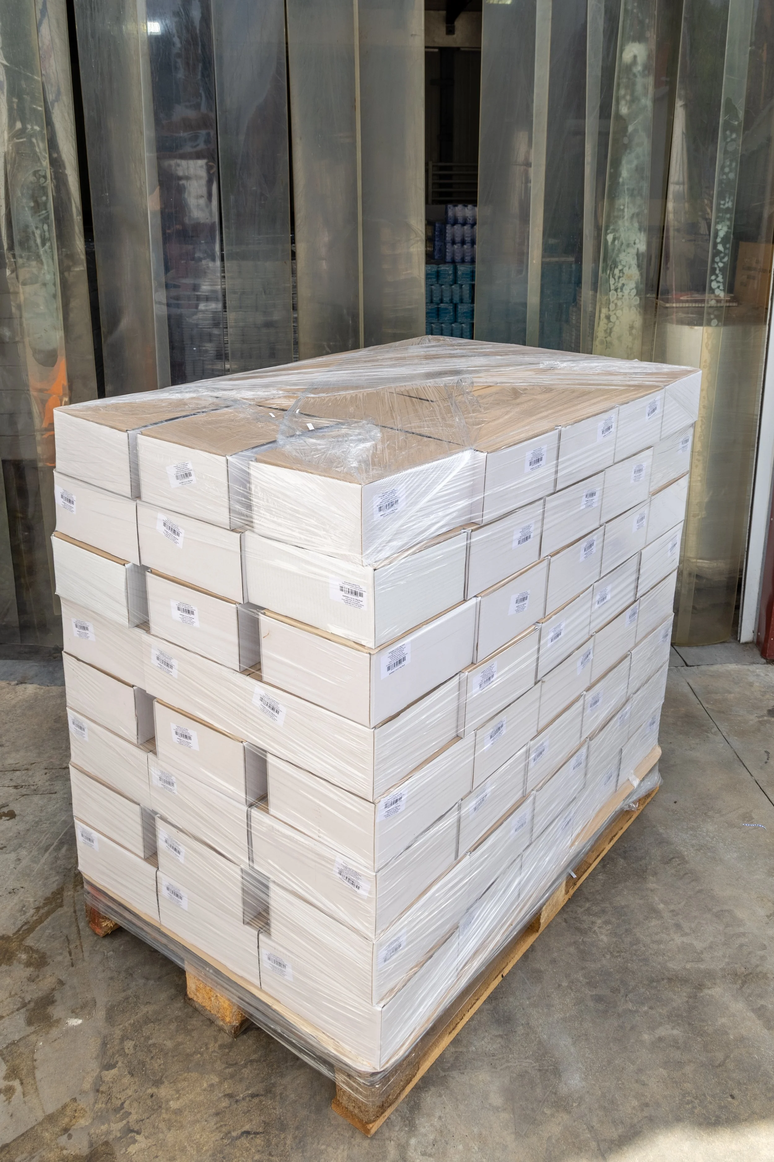 Stack of white boxes wrapped in plastic on a wooden pallet outside a store.