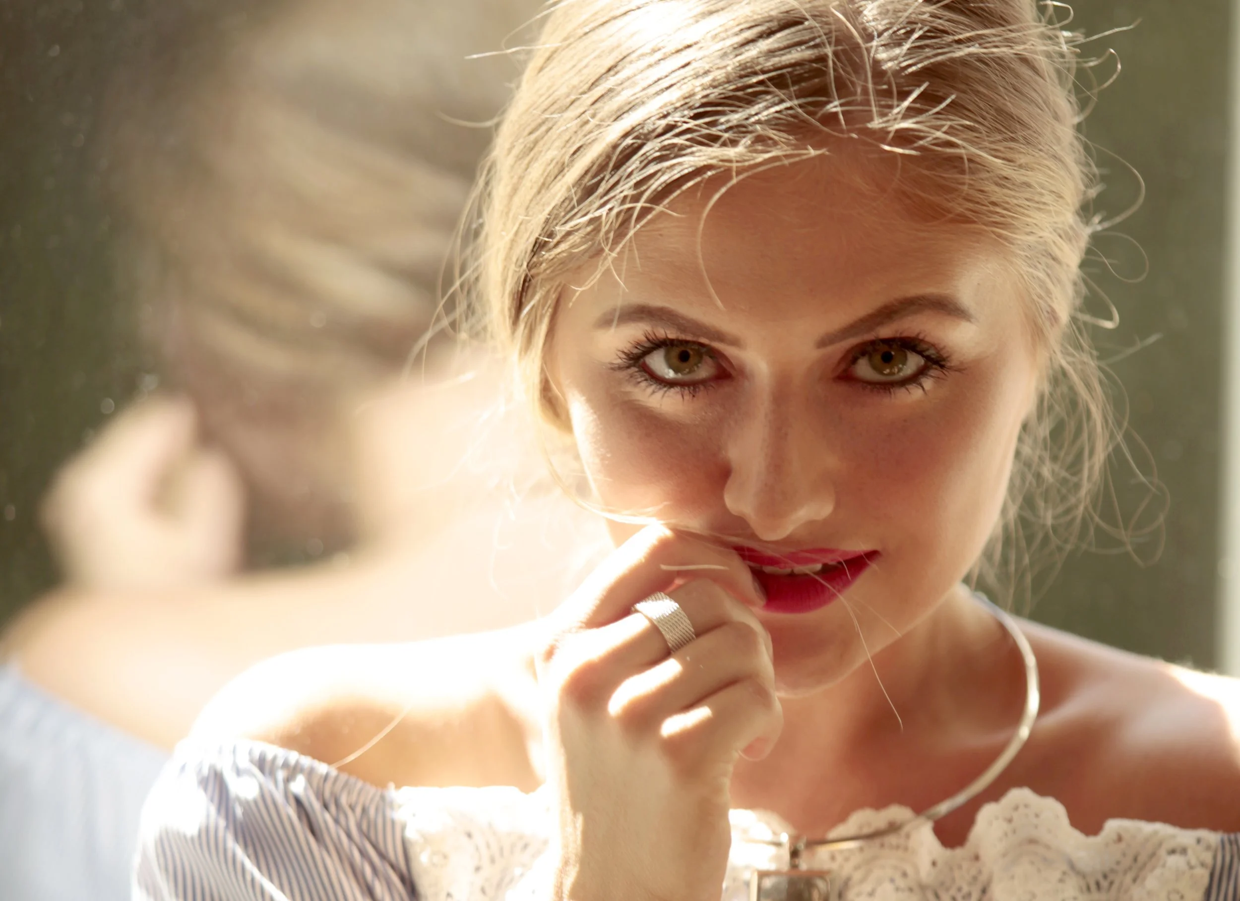 Nahaufnahme eines lachenden Mädchens mit blonden Haaren und braunen Augen, das eine Hand an das Gesicht hält.