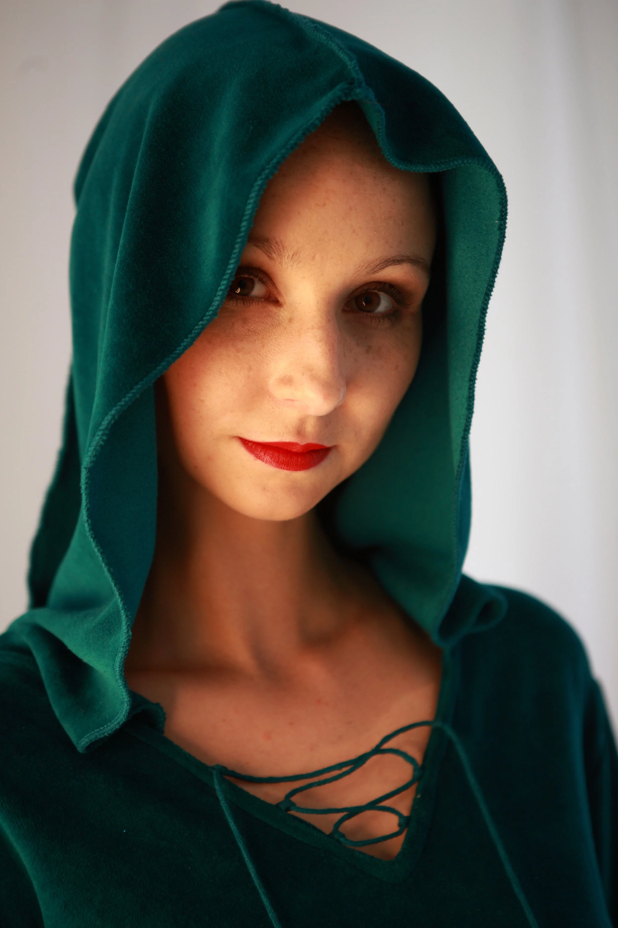 Porträt einer Frau mit rotem Lippenstift, die einen grünen Hoodie trägt, der die Hälfte ihres Gesichts bedeckt, und im Profil nach rechts schaut.