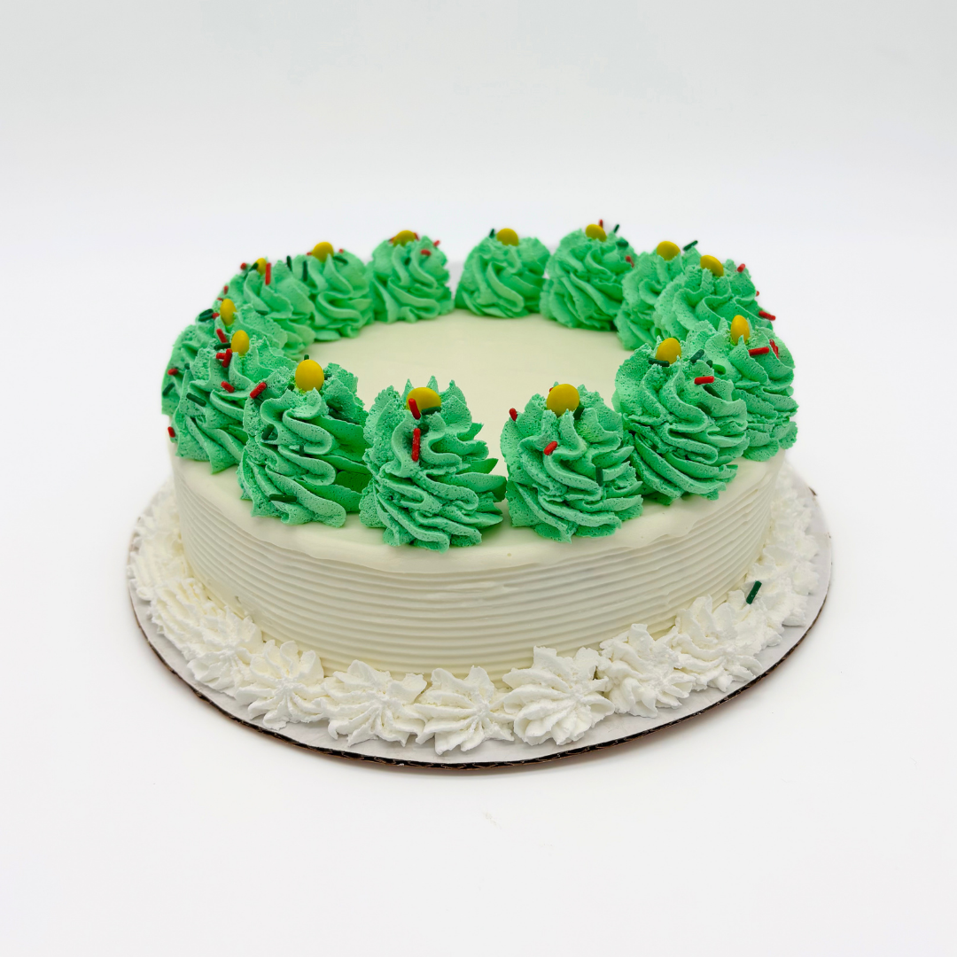 White cake with white frosted sides, decorated with green whipped cream swirls on top, topped with small yellow and red sprinkles.