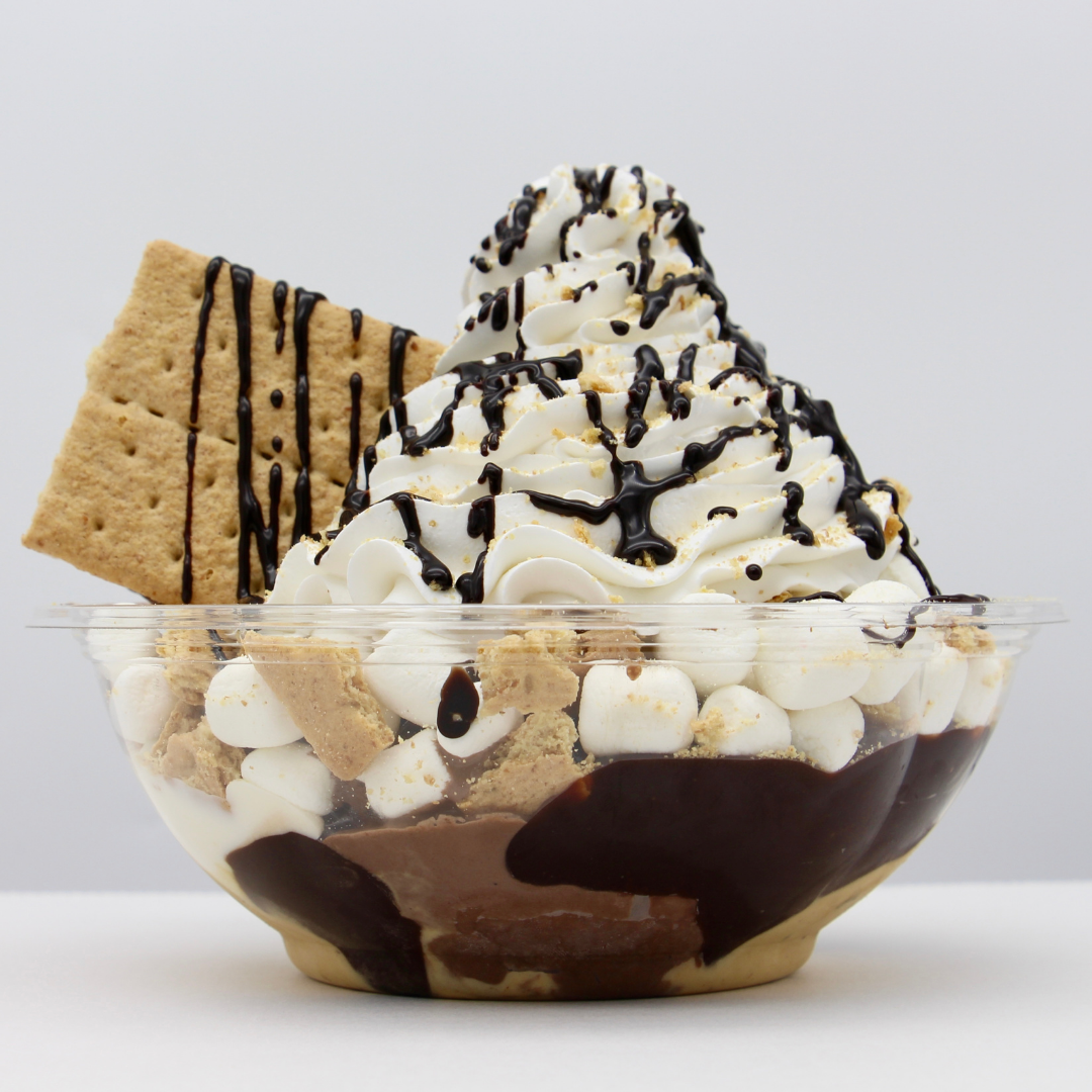 Chocolate sundae in a clear glass bowl topped with whipped cream, chocolate syrup, marshmallows, and graham crackers, with graham crackers and cookies on the side.