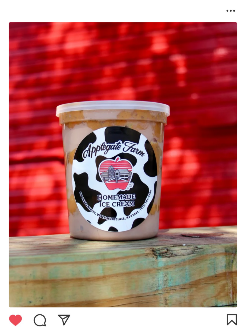A container of homemade ice cream from Applegate Farm with a black and white cow print design, placed on a wooden surface against a red brick background.