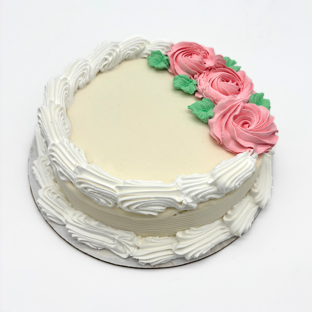 A round white cake decorated with white cream piping around the edges and pink roses with green leaves on top.