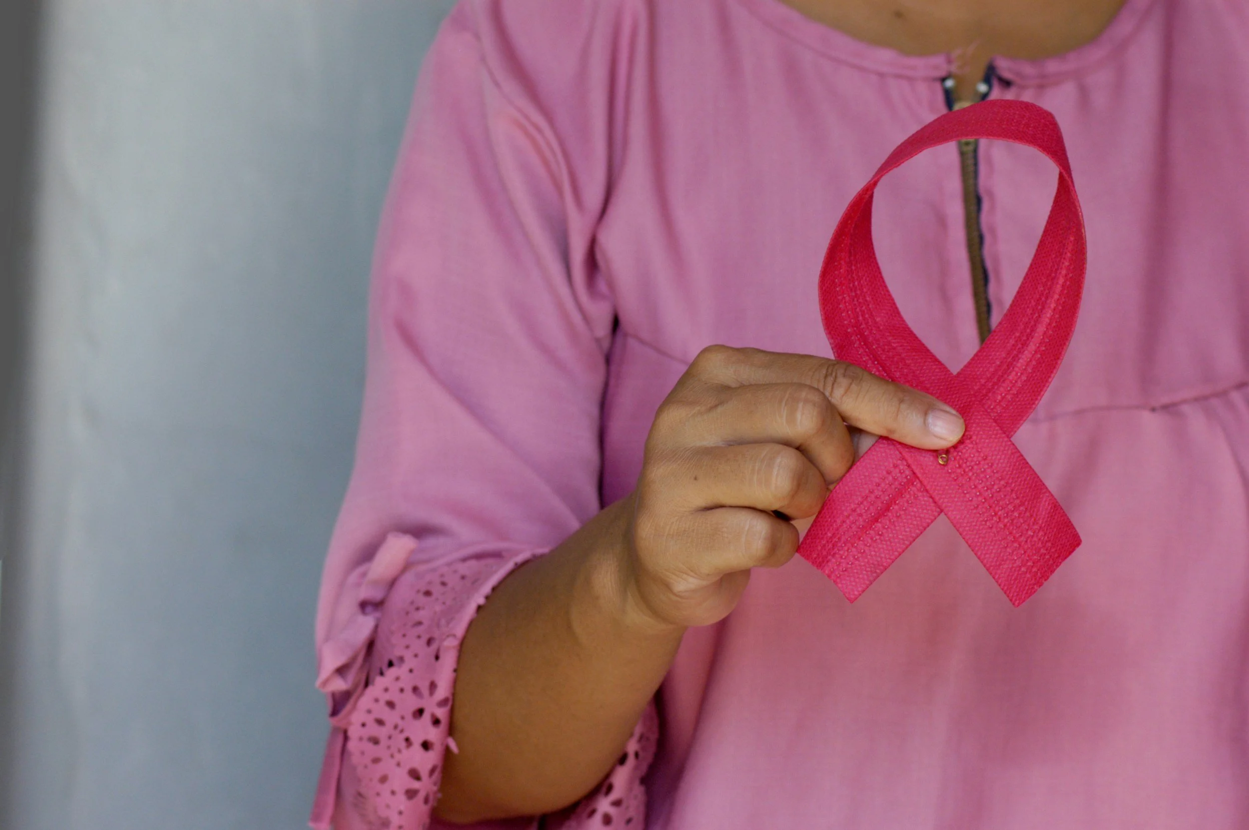 A person wearing a pink top holding a pink ribbon, symbol of breast cancer awareness.