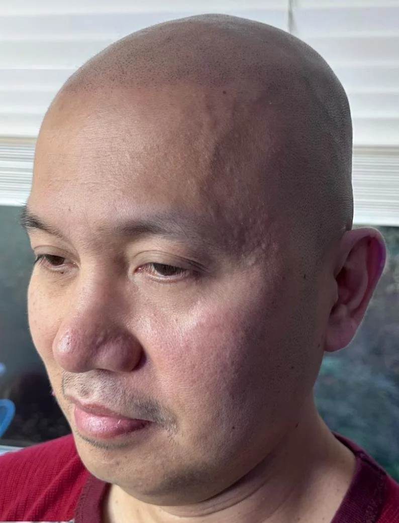 Close-up photo of a man with a shaved head and slightly closed eyes, wearing a red shirt.