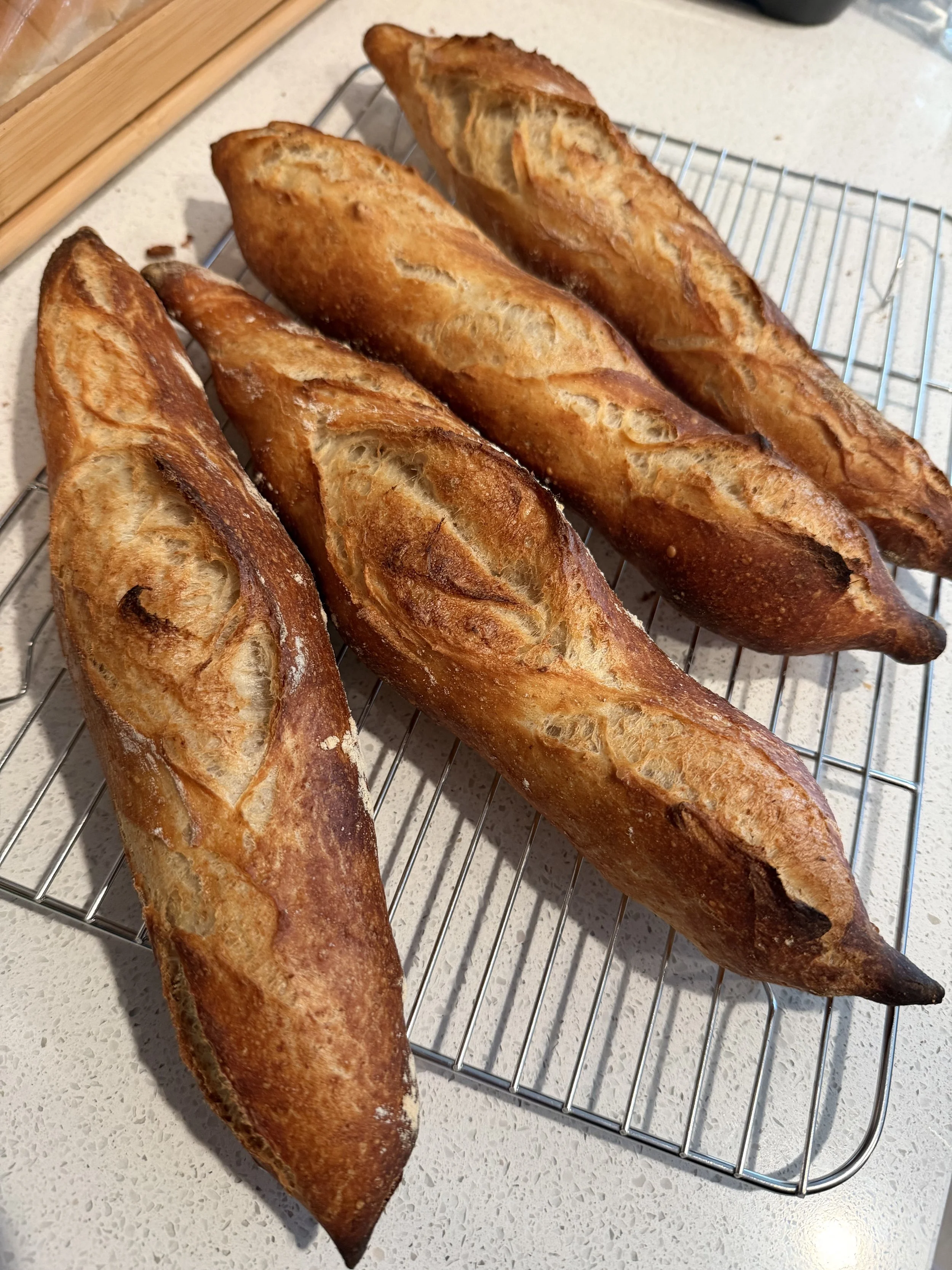 Four baguette loaves of bread resting on a cooling rack on a kitchen countertop.