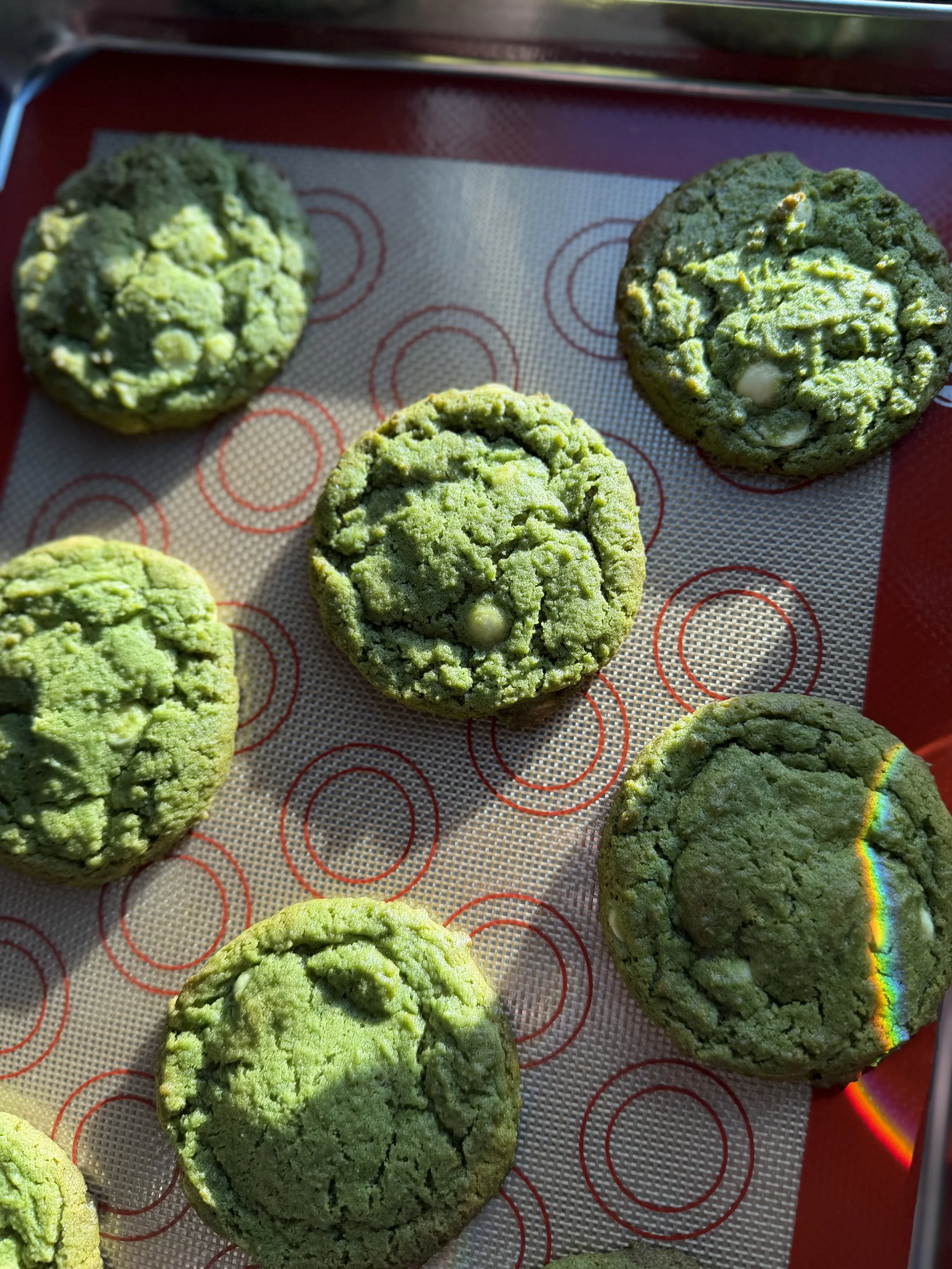 Several green cookies with cracked surfaces on a red tray lined with white paper with red circles, outdoors in sunlight.