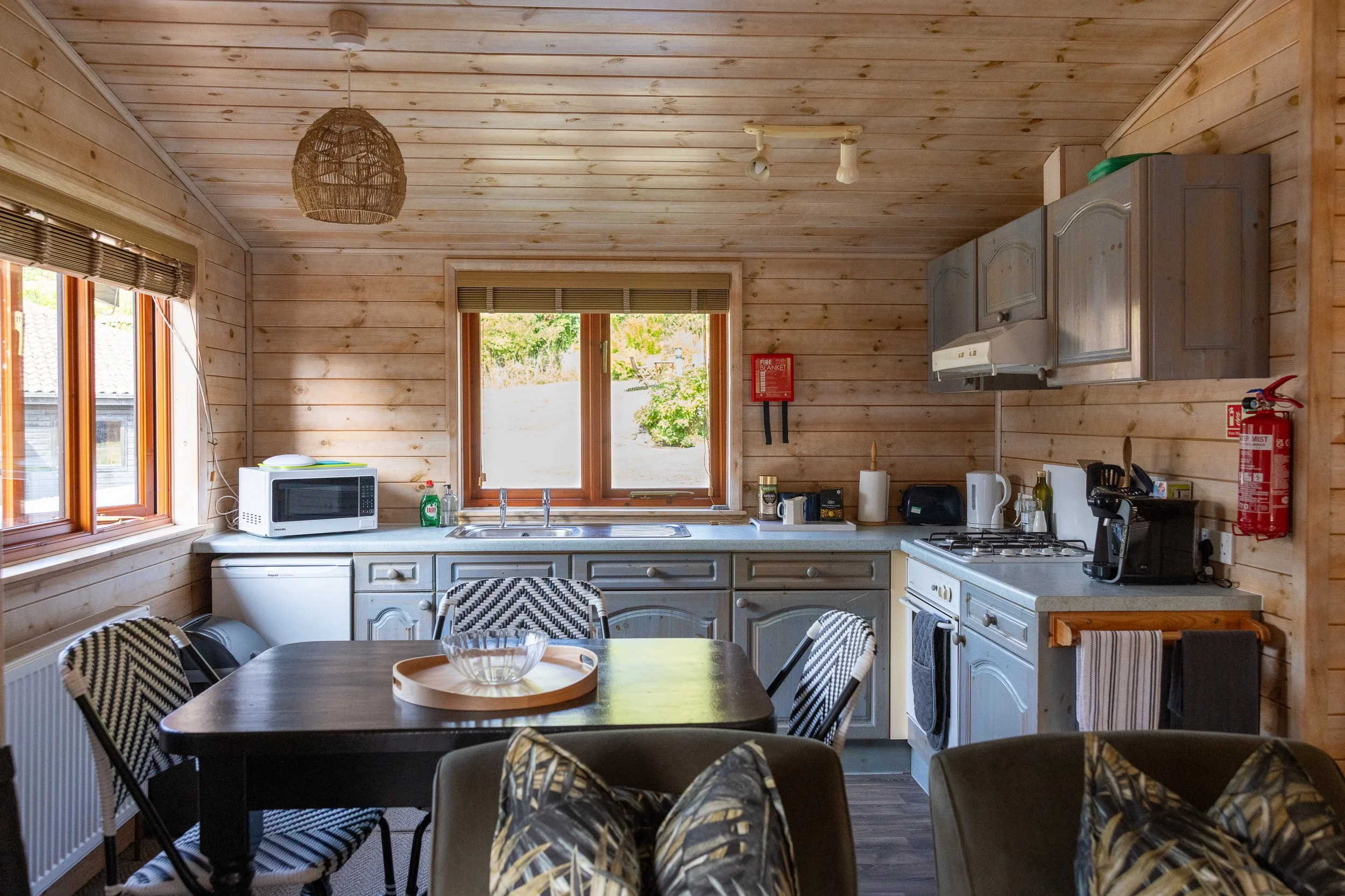 Kitchen with wood-paneled walls and ceiling, featuring gray cabinets, a stove, microwave, and dining table with chairs.