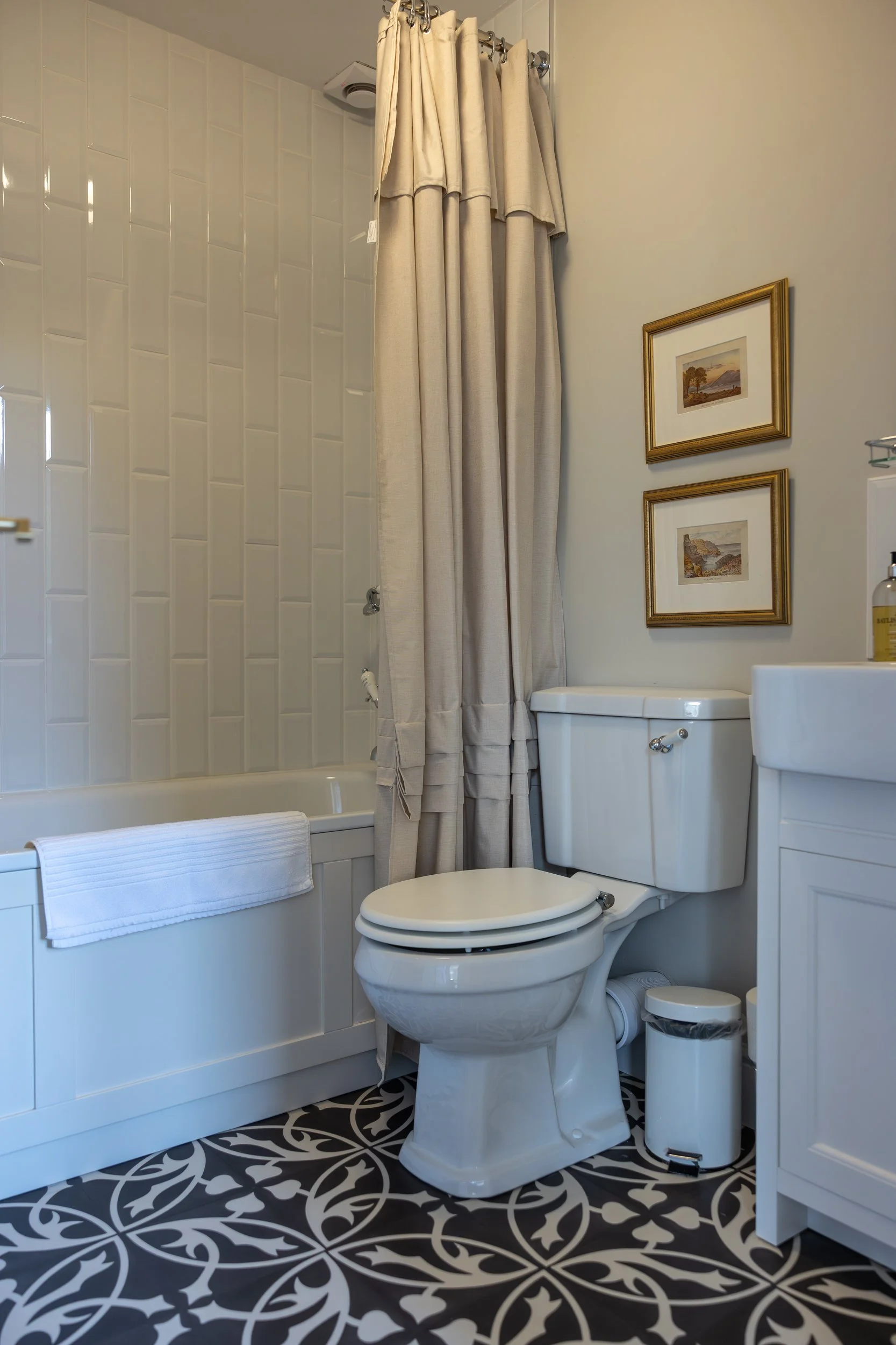Bathroom with a bathtub and shower, a toilet, a small sink, and framed pictures on the wall.
