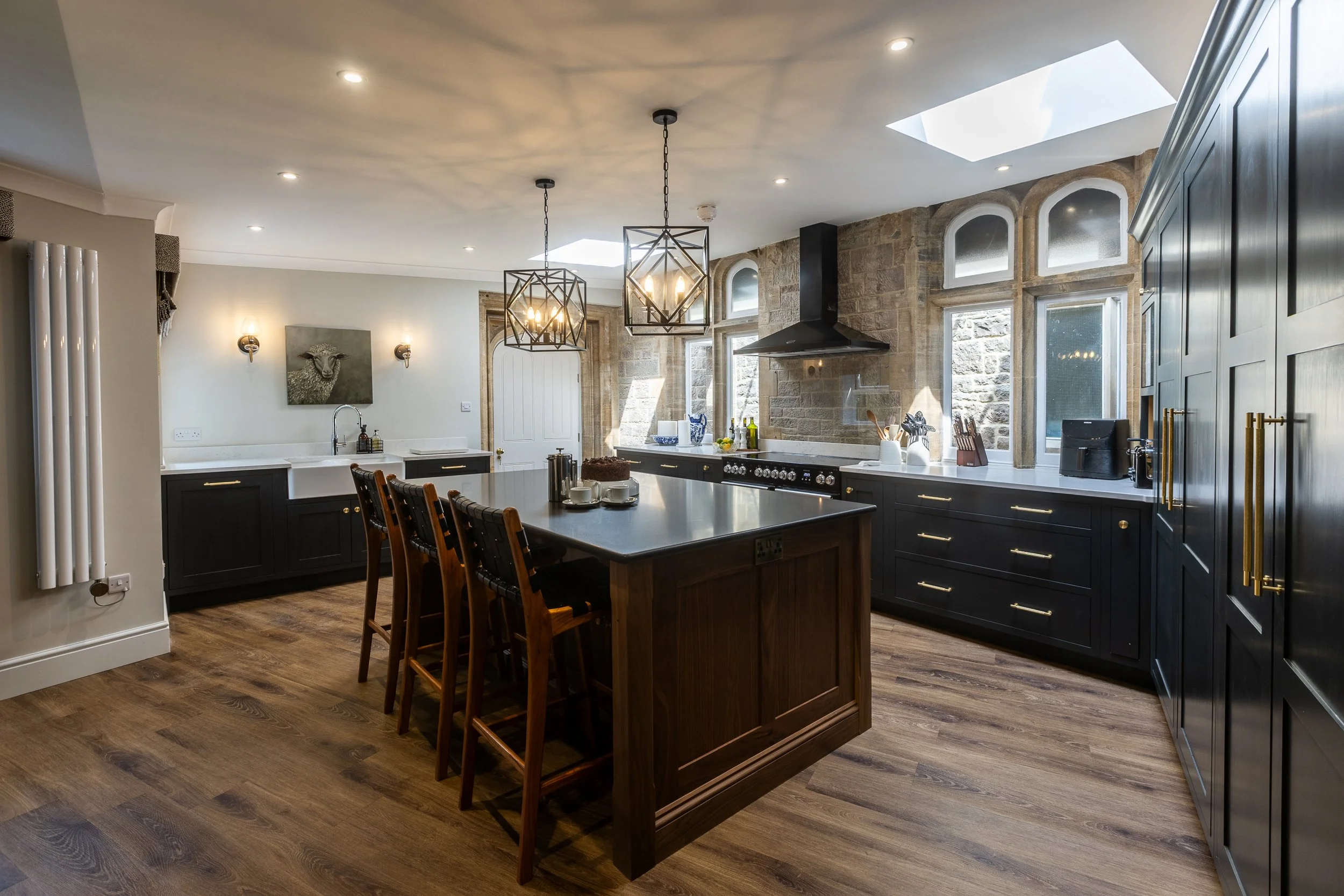 Kitchen with dark cabinets, a large kitchen island with barstools, stone walls, multiple windows, skylights, and pendant lighting