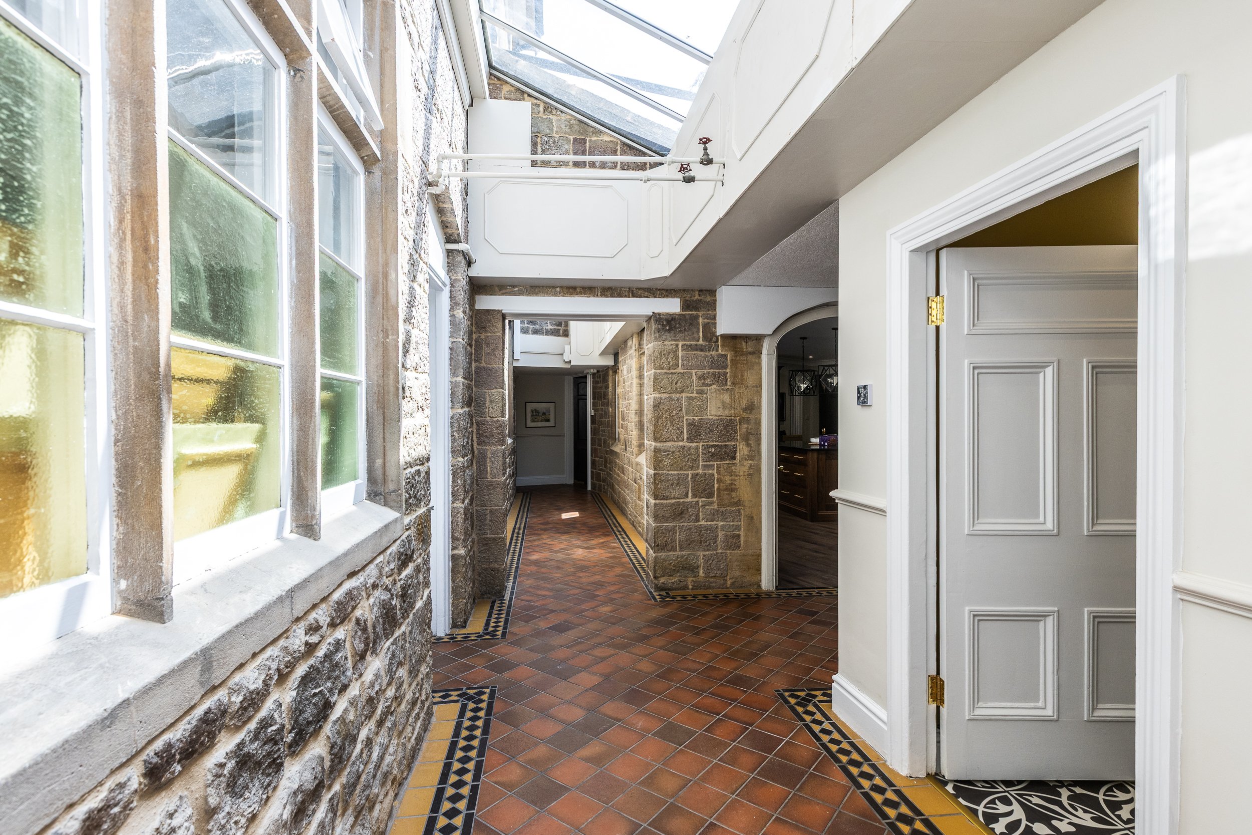 Interior view of a hallway with brick walls, a skylight ceiling, and a tiled floor with decorative border patterns.