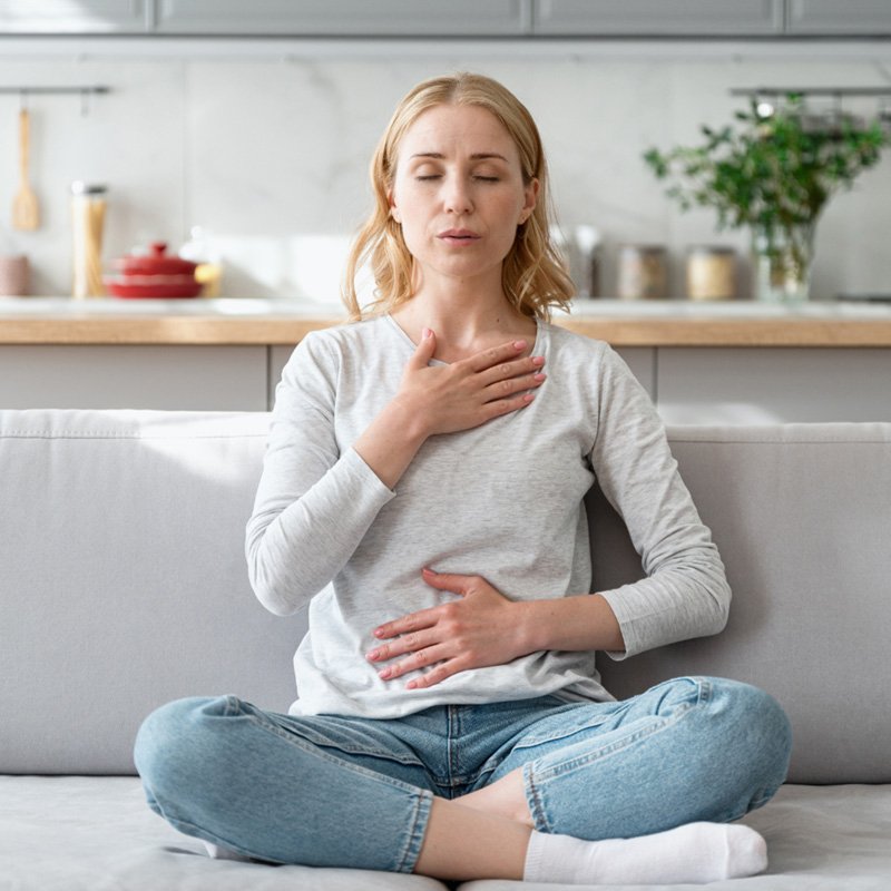 Woman practicing diaphragmatic belly breathing while seated cross-legged at home