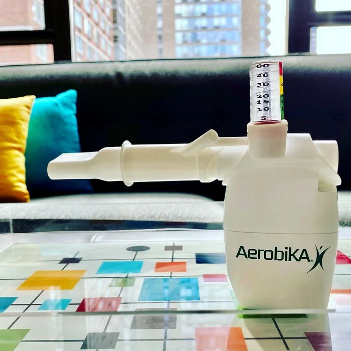 Aerobika by Trudell and Monaghan medical with a manometer and a sofa with blue and yellow pillows behind it