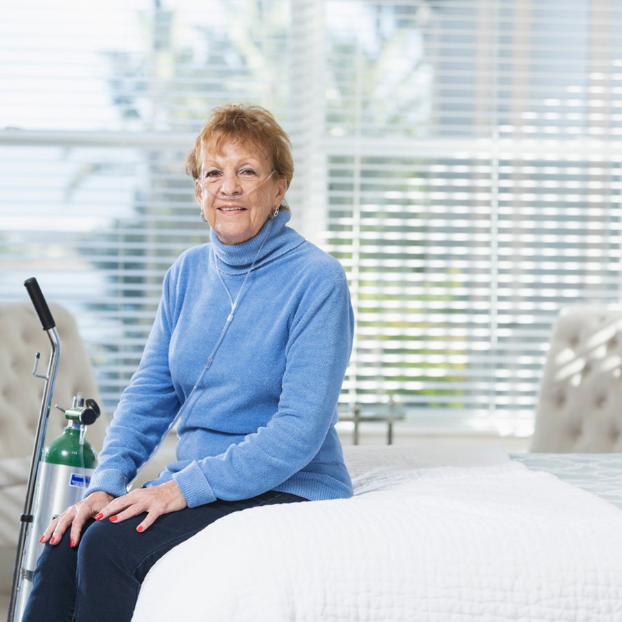 Woman using a portable oxygen tank and nasal cannula while sitting on her bed