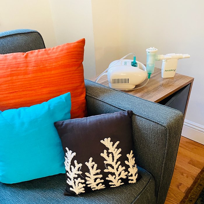 Monaghan Medical Aerobika and AeroEclipse nebulizer on table with colorful pillows next to it on sofa