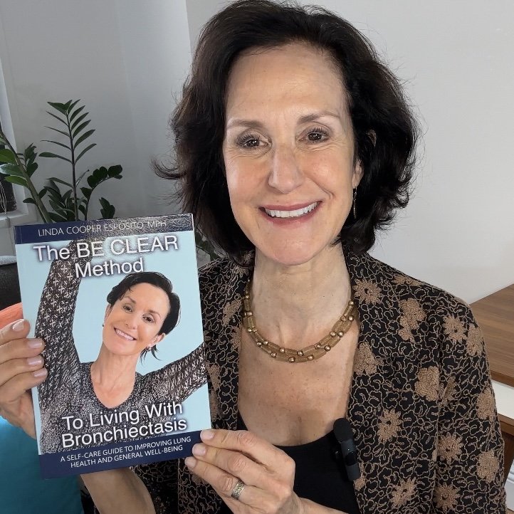 Linda Esposito holding her book, The BE CLEAR Method to Living with Bronchiectasis and smiling