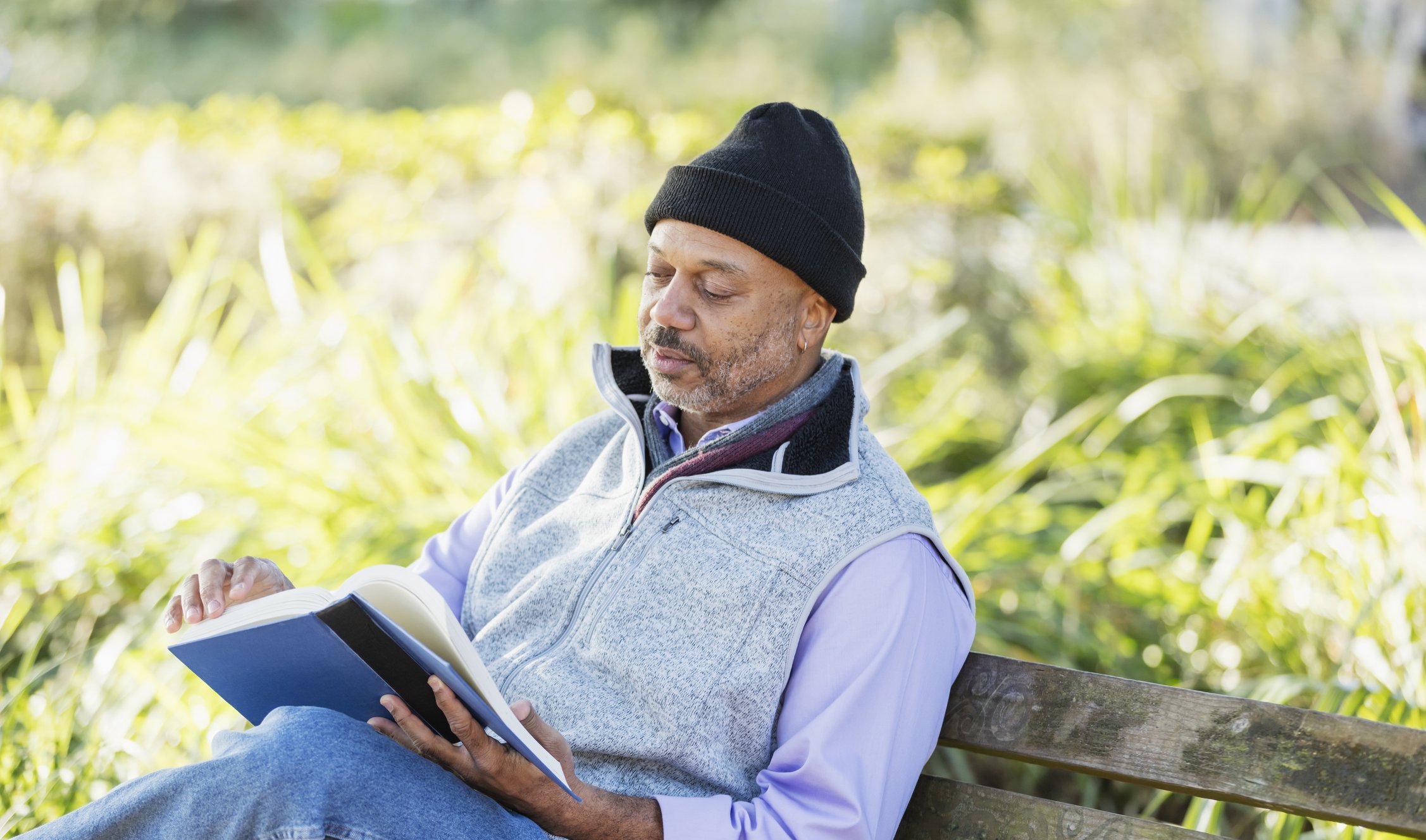 Man resting on a park bench while reading a book, prioritizing rest and recovery