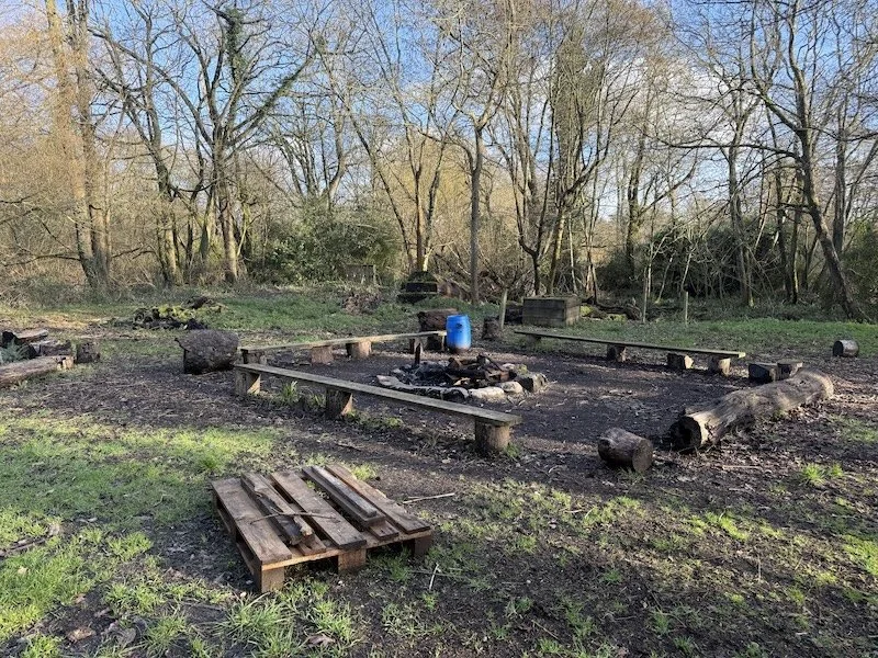 Two individuals wearing sumo wrestler costumes engaging in a sumo match on a mat at a Scout Camp. In the background, there are inflatables and people attending the event on a sunny day.
