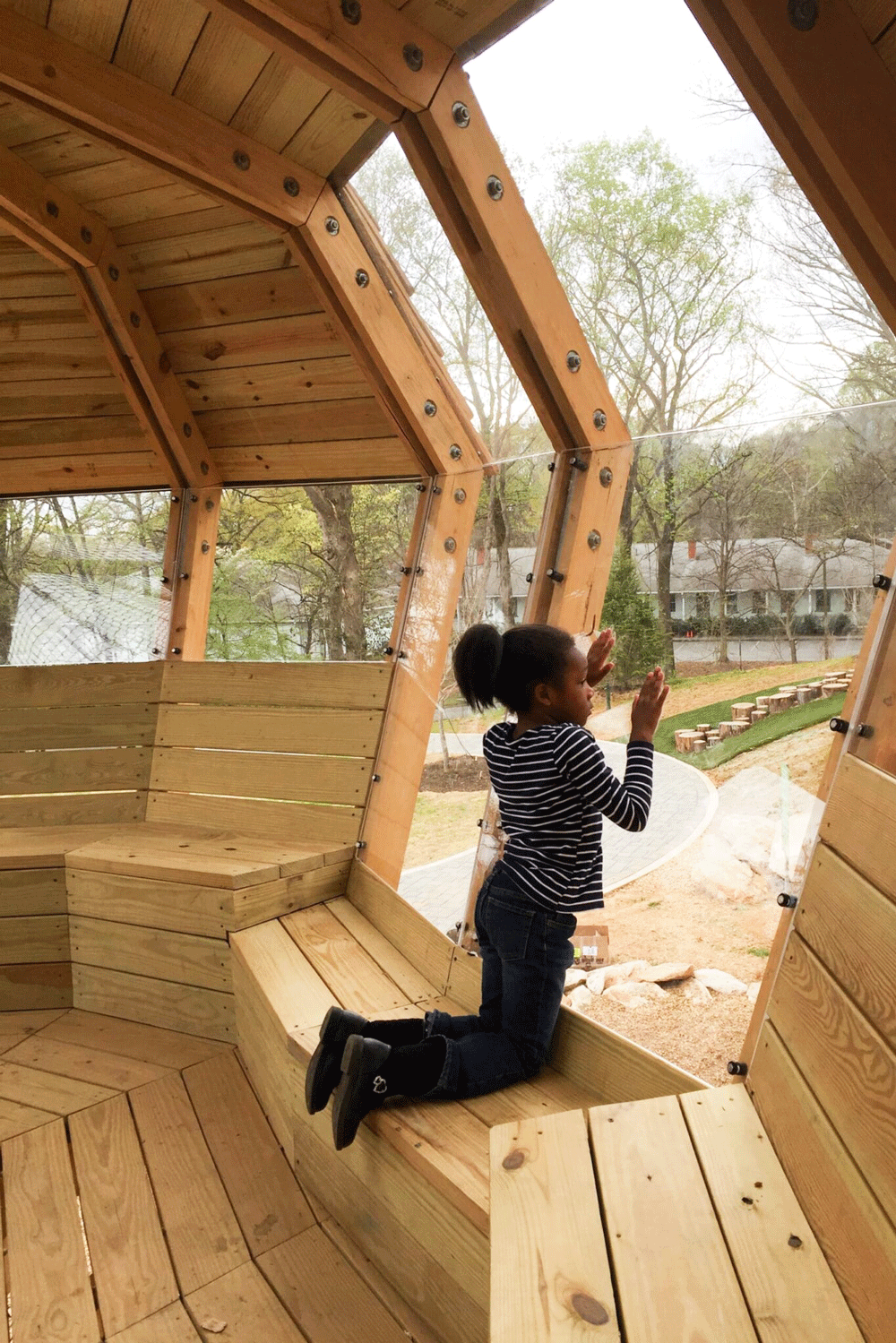 Child observing park from treehouse window