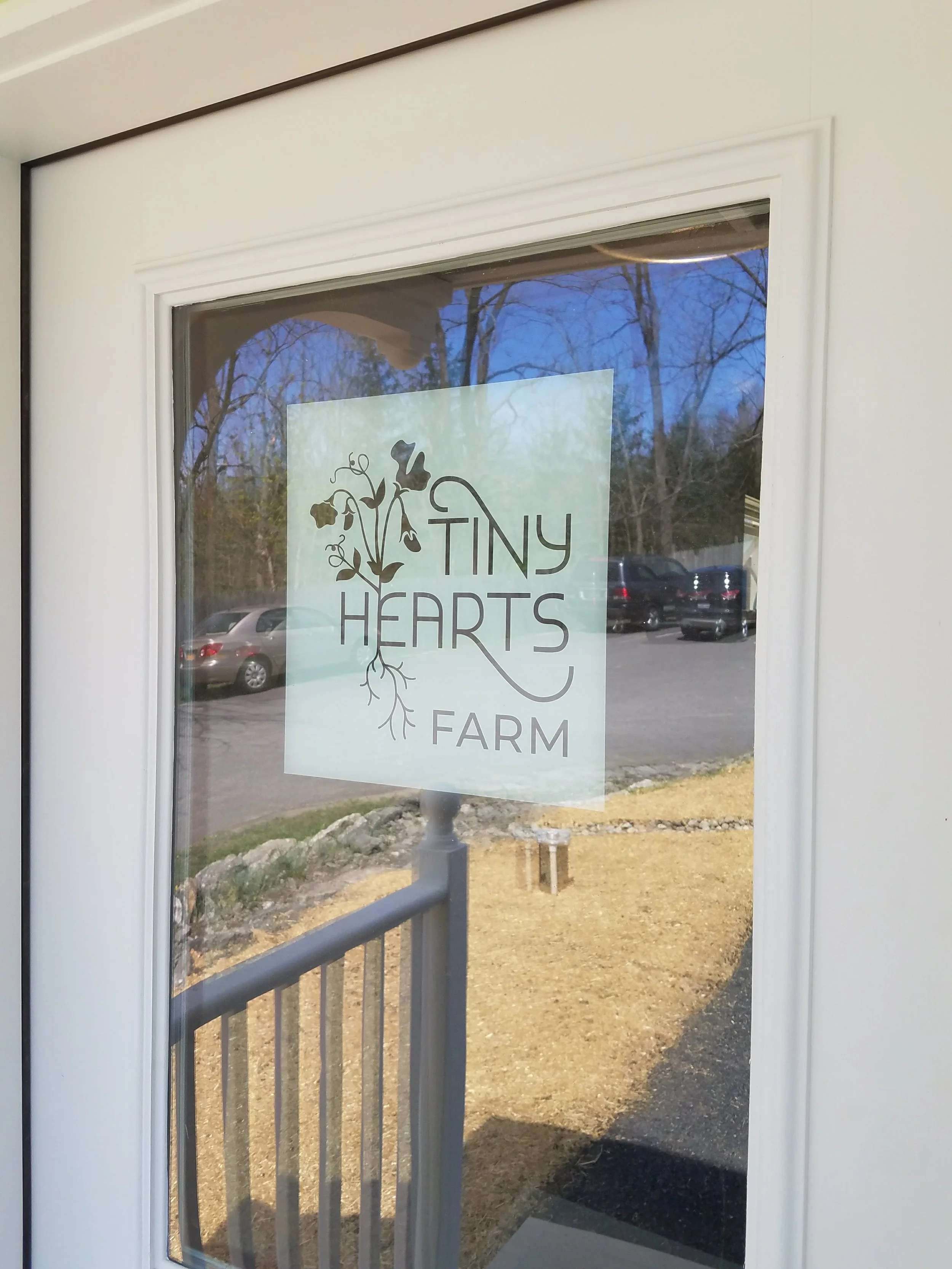 Sign on glass door for Tiny Hearts Farm featuring a floral design.